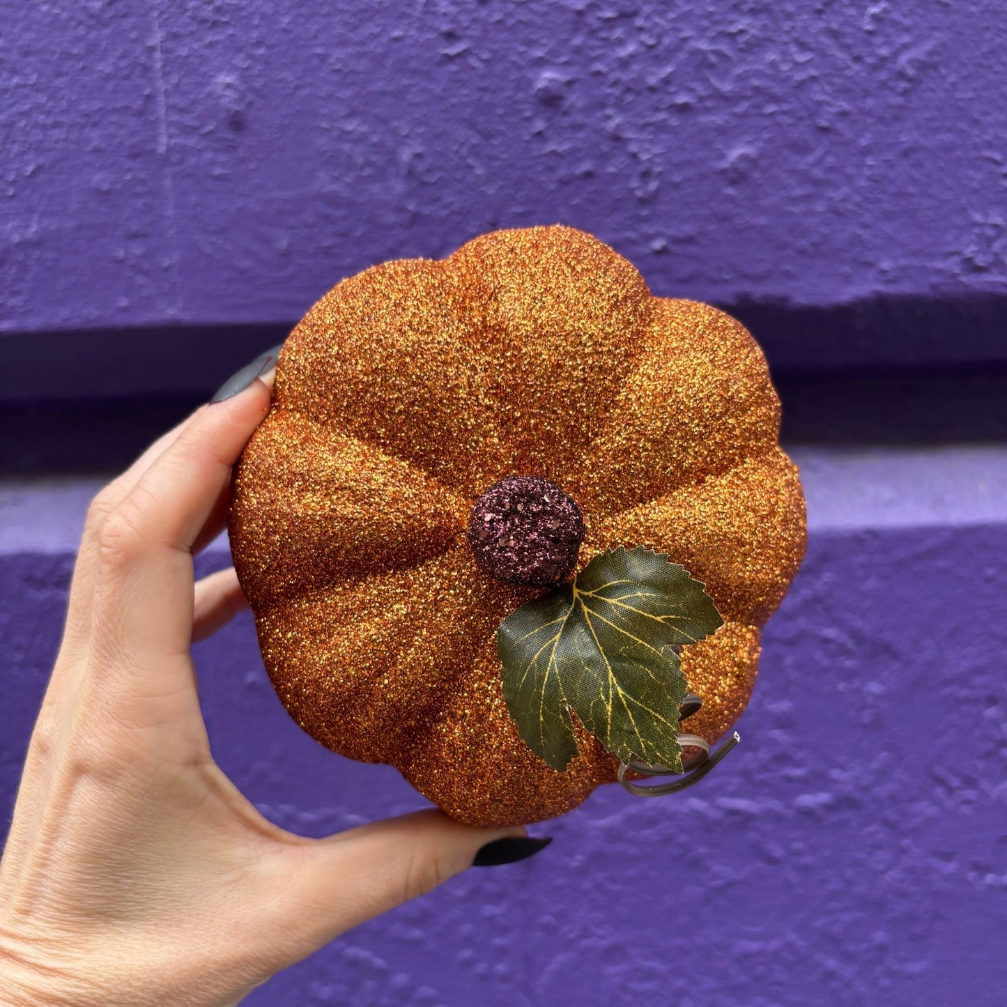 Hand holding a glittery pumpkin against a purple background