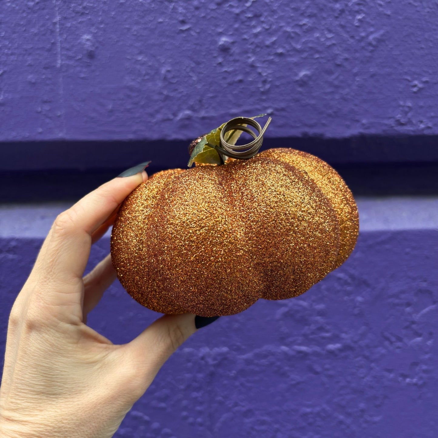Hand holding a glittery gold pumpkin against a purple wall