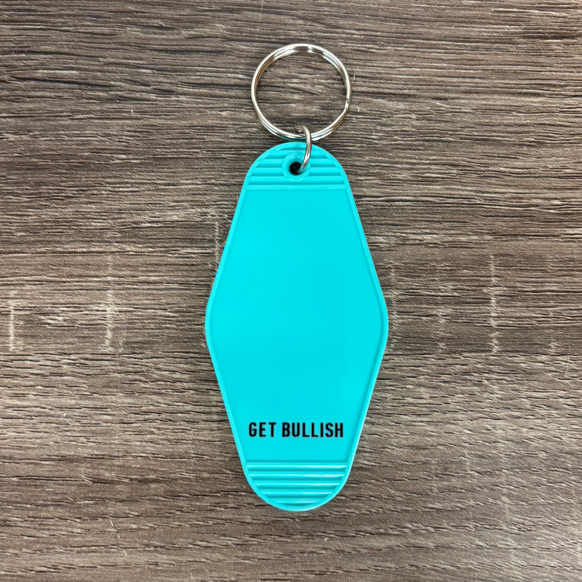 Turquoise keychain with 'GET BULLISH' text on a wooden surface