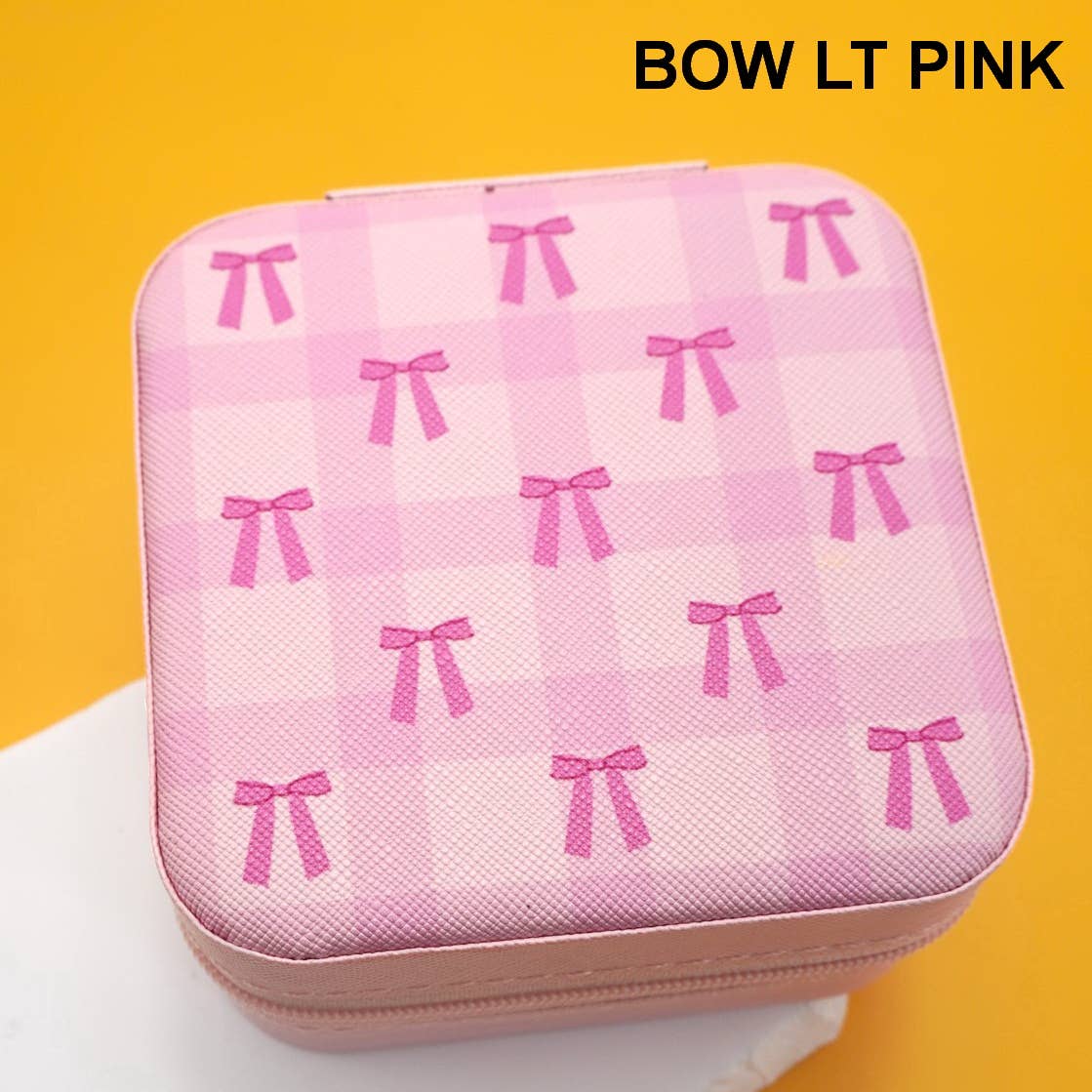 A square pink zippered jewelry box with a light pink and white gingham pattern and pink bow motifs