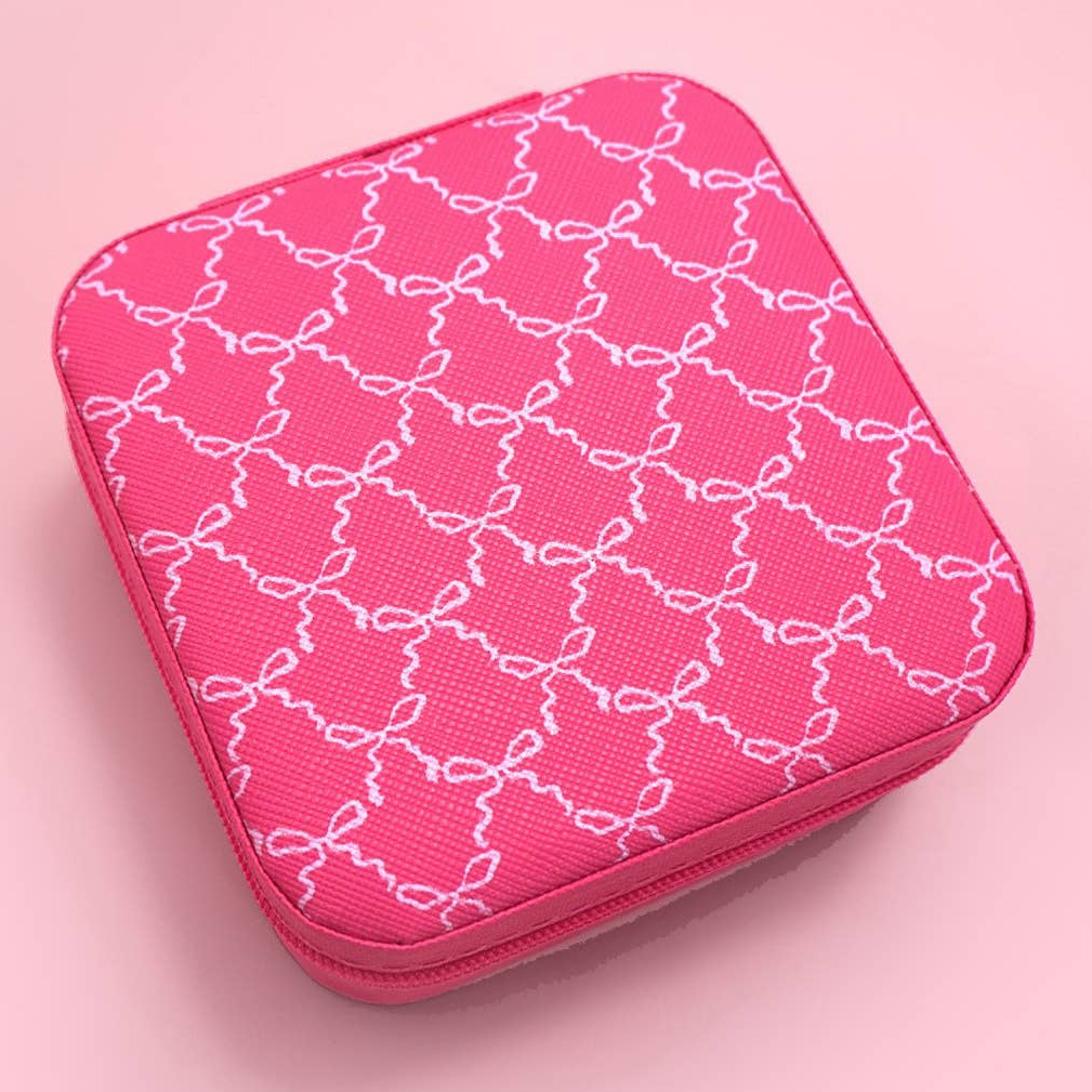 A square pink zippered jewelry box with rounded corners, featuring a white repeating bow pattern on a textured fabric surface.
