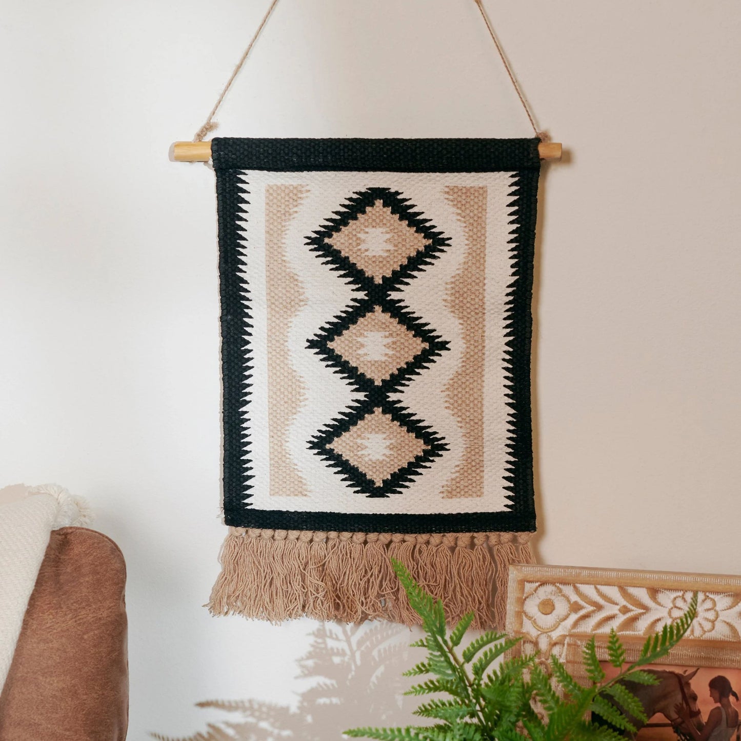 Woven wall hanging with geometric pattern and tassels on a neutral background