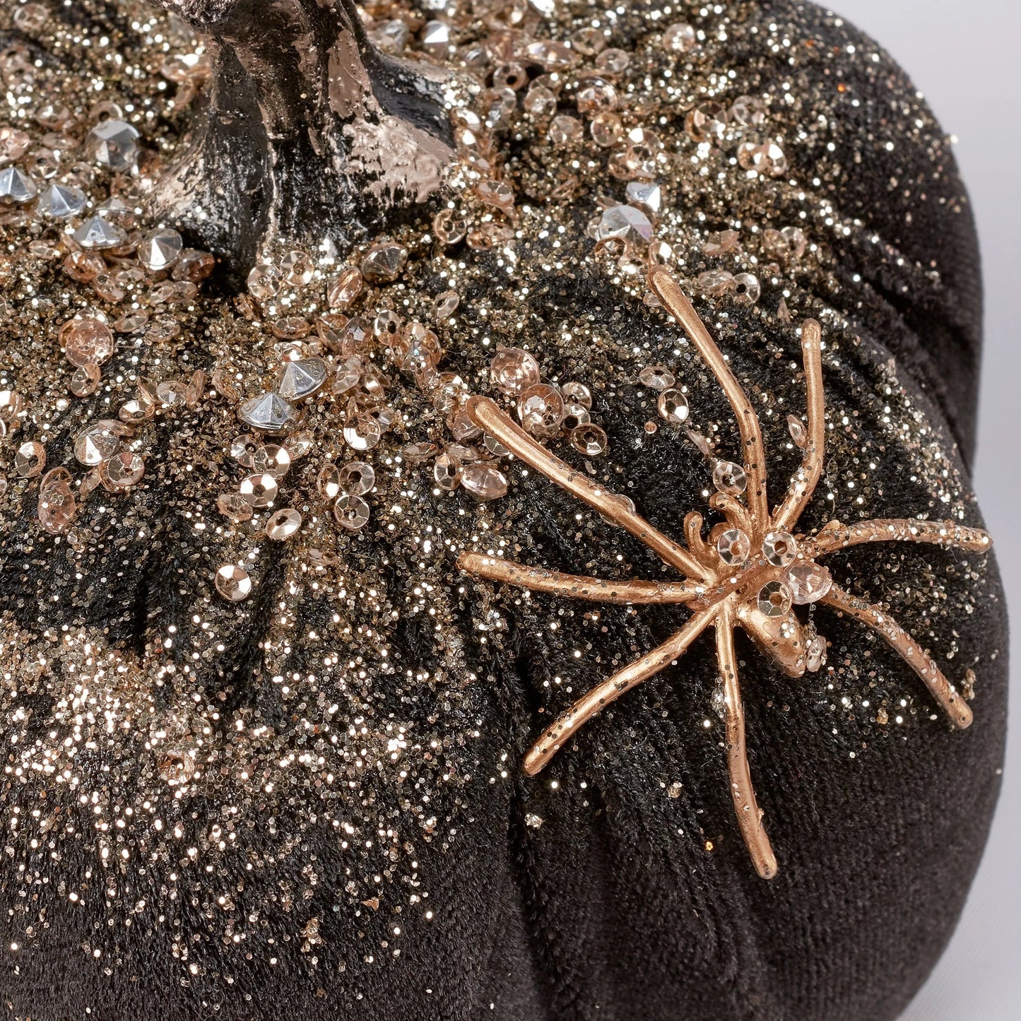 Bronze spider figurine on a textured black surface with glittery accents