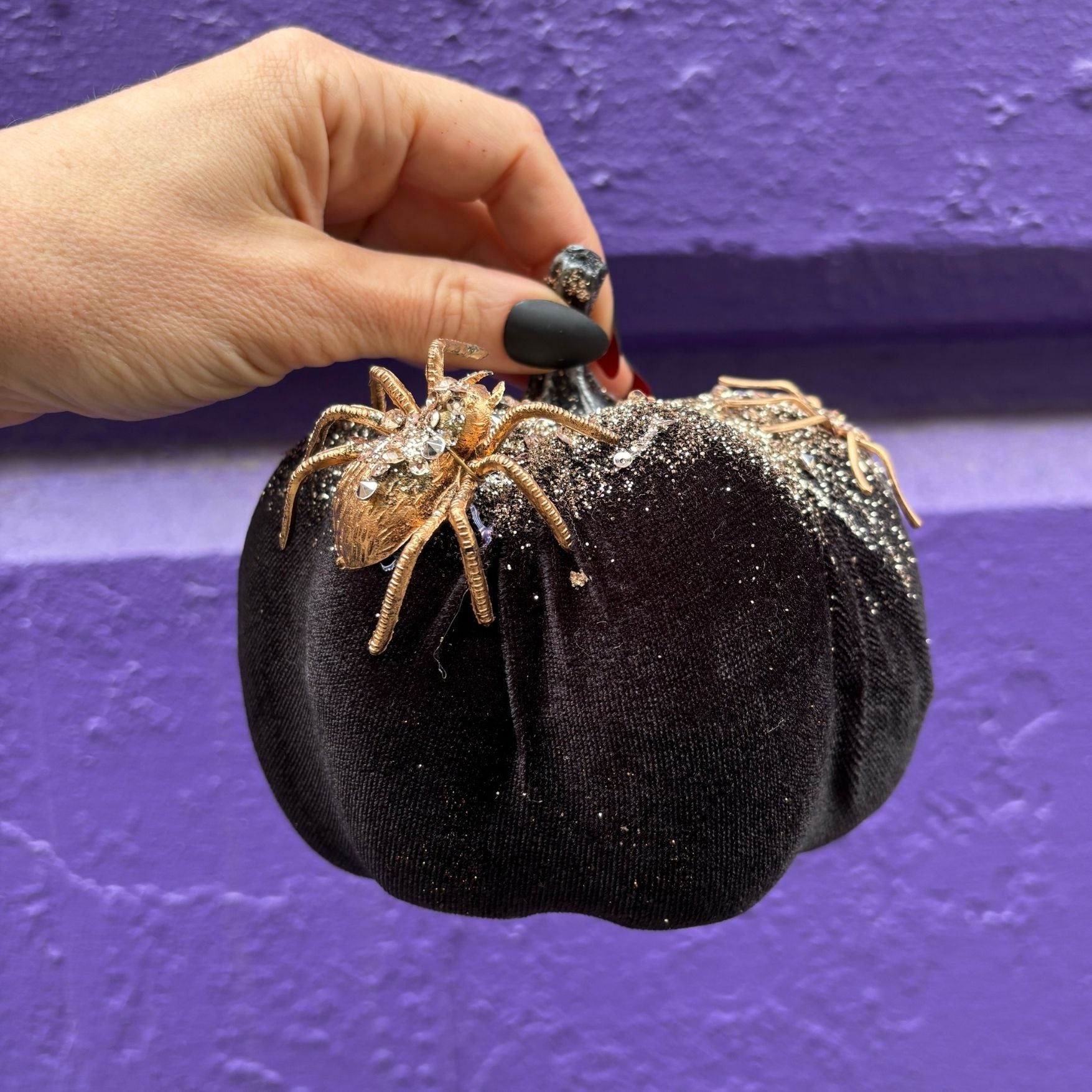 Black glittery pumpkin with a spider decoration against a purple background