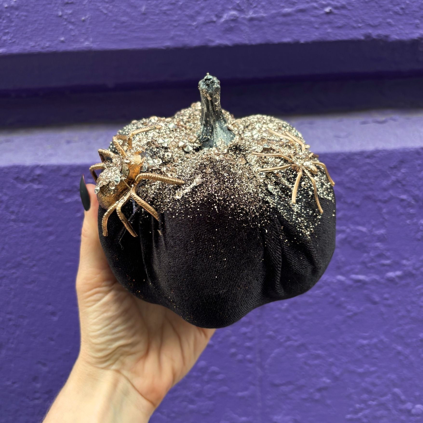 Decorative pumpkin with glitter and spider decorations held against a purple background