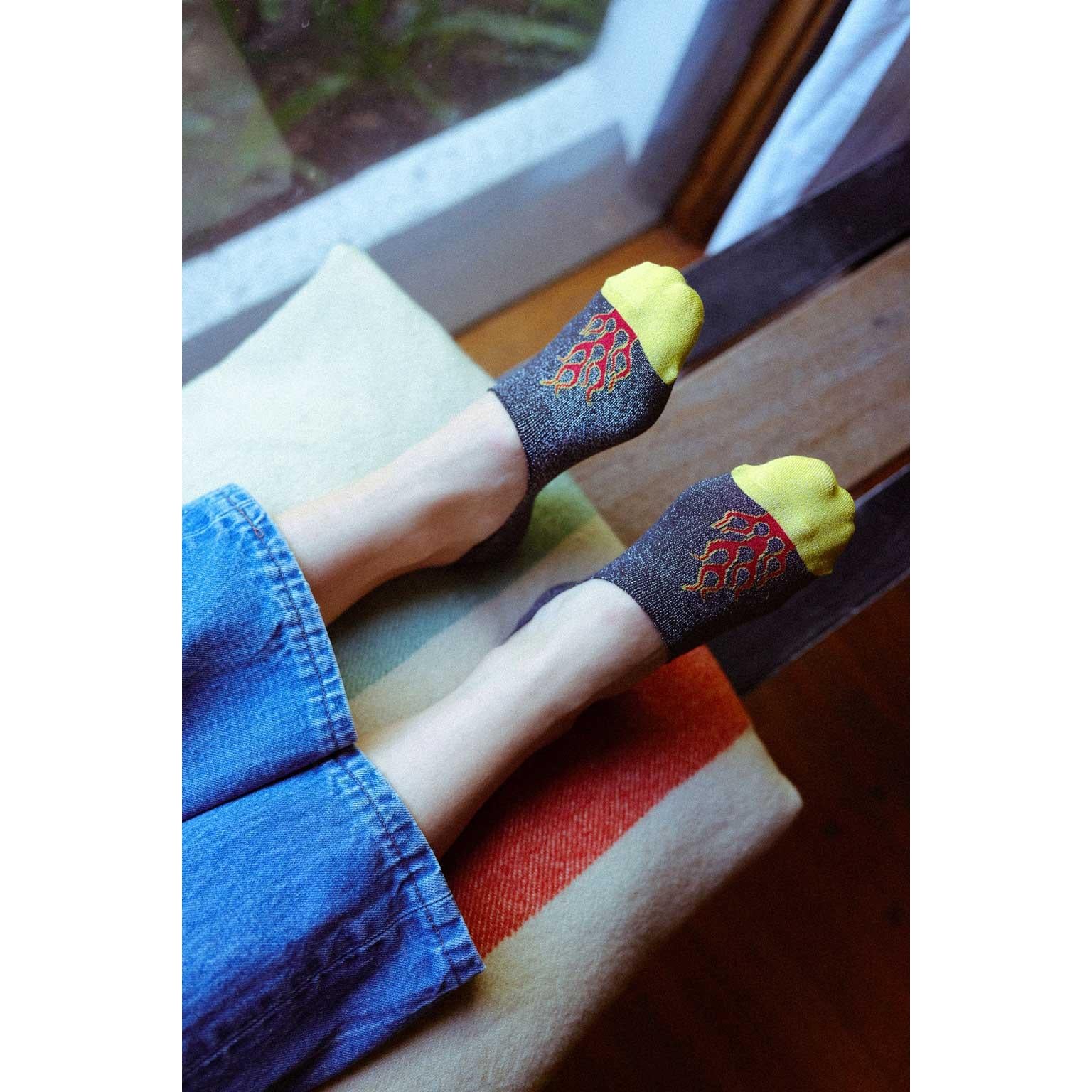 Person wearing no-show socks with flame design and yellow toes, sitting on a wooden bench.