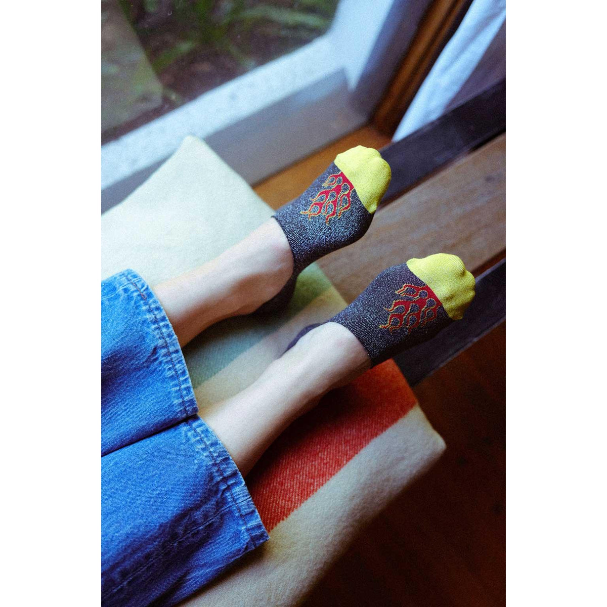Person wearing no-show socks with flame design and yellow toes, sitting on a wooden bench.