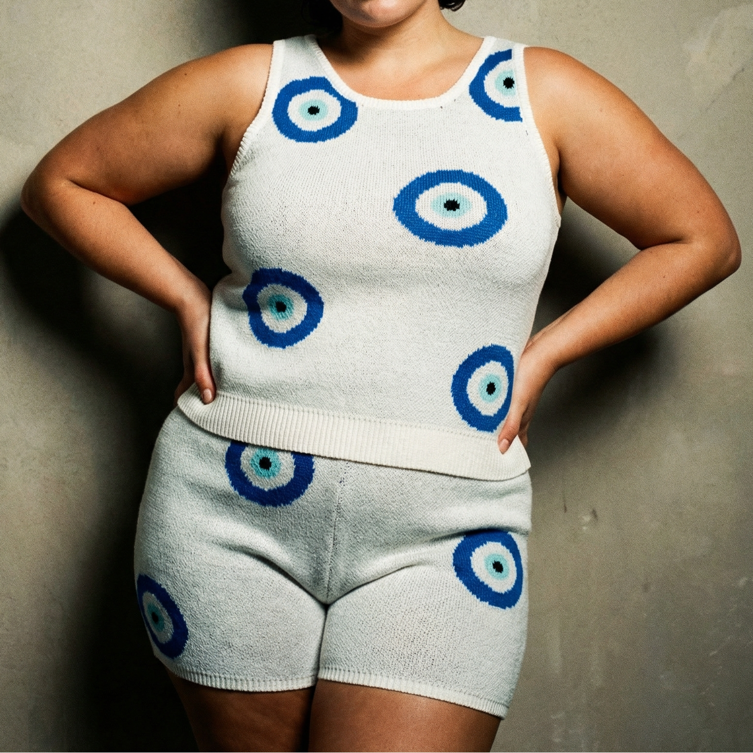 Person wearing a white tank top and shorts with blue and green circle patterns against a plain background