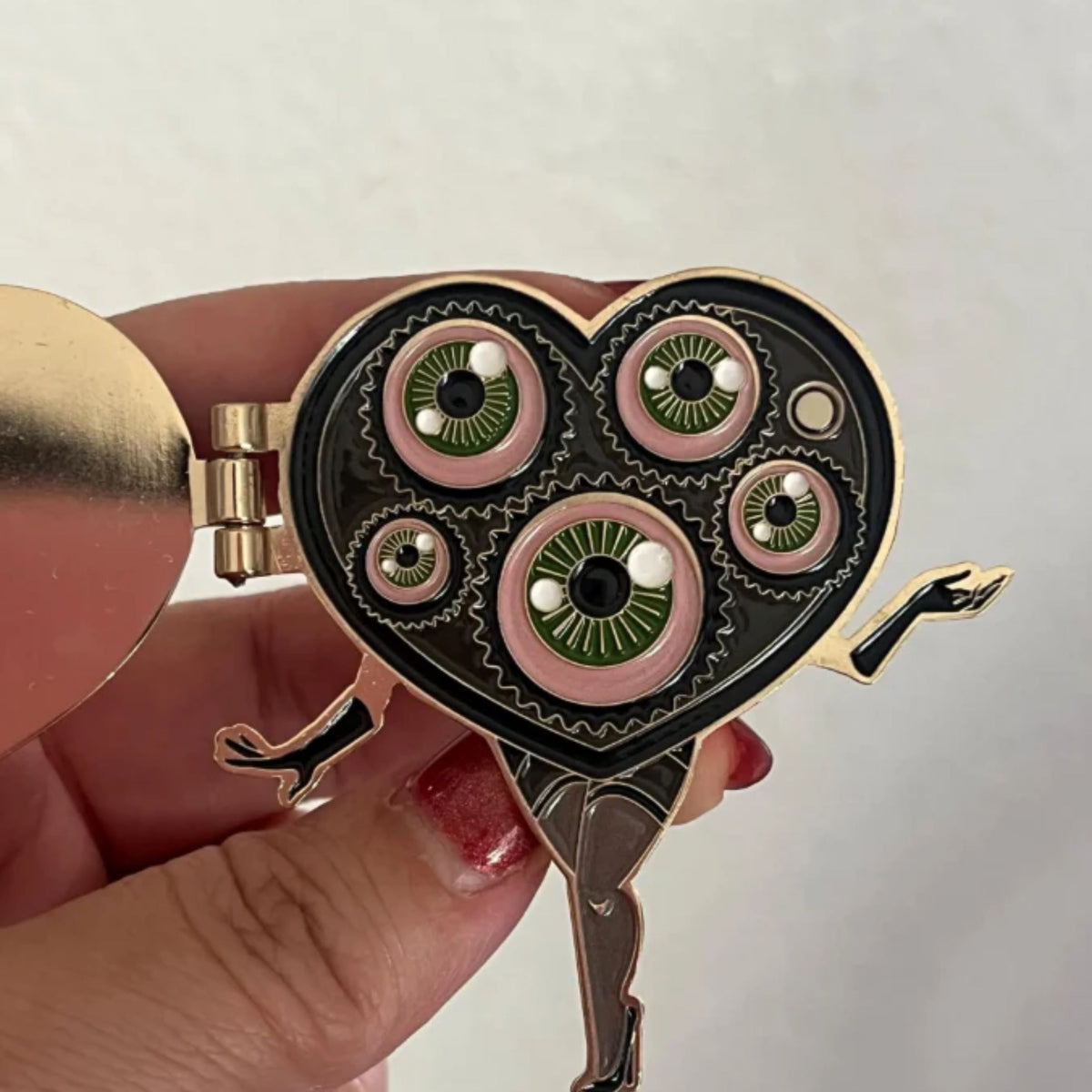 Hinged heart-shaped pin with multiple eyes held by a hand against a neutral background