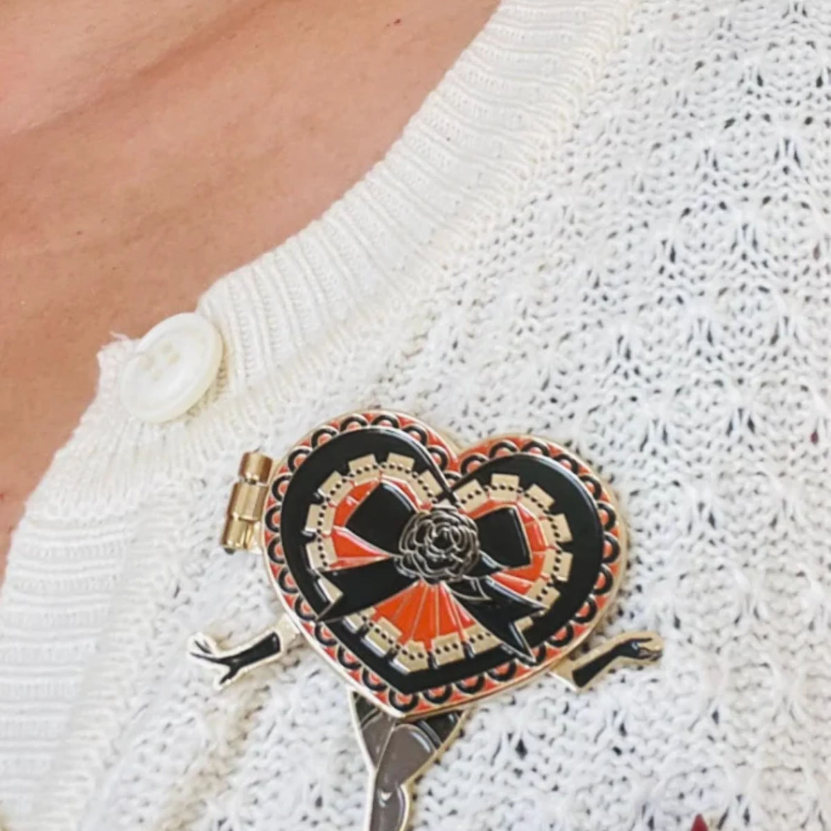 Heart-shaped brooch with black ribbon design on a white textured sweater