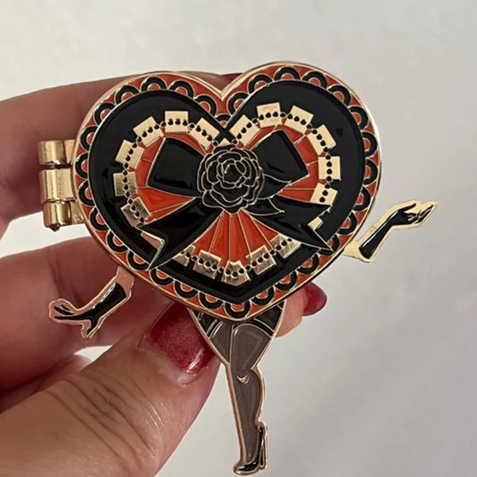 Heart-shaped decorative enamel pin with a rose design held by a hand