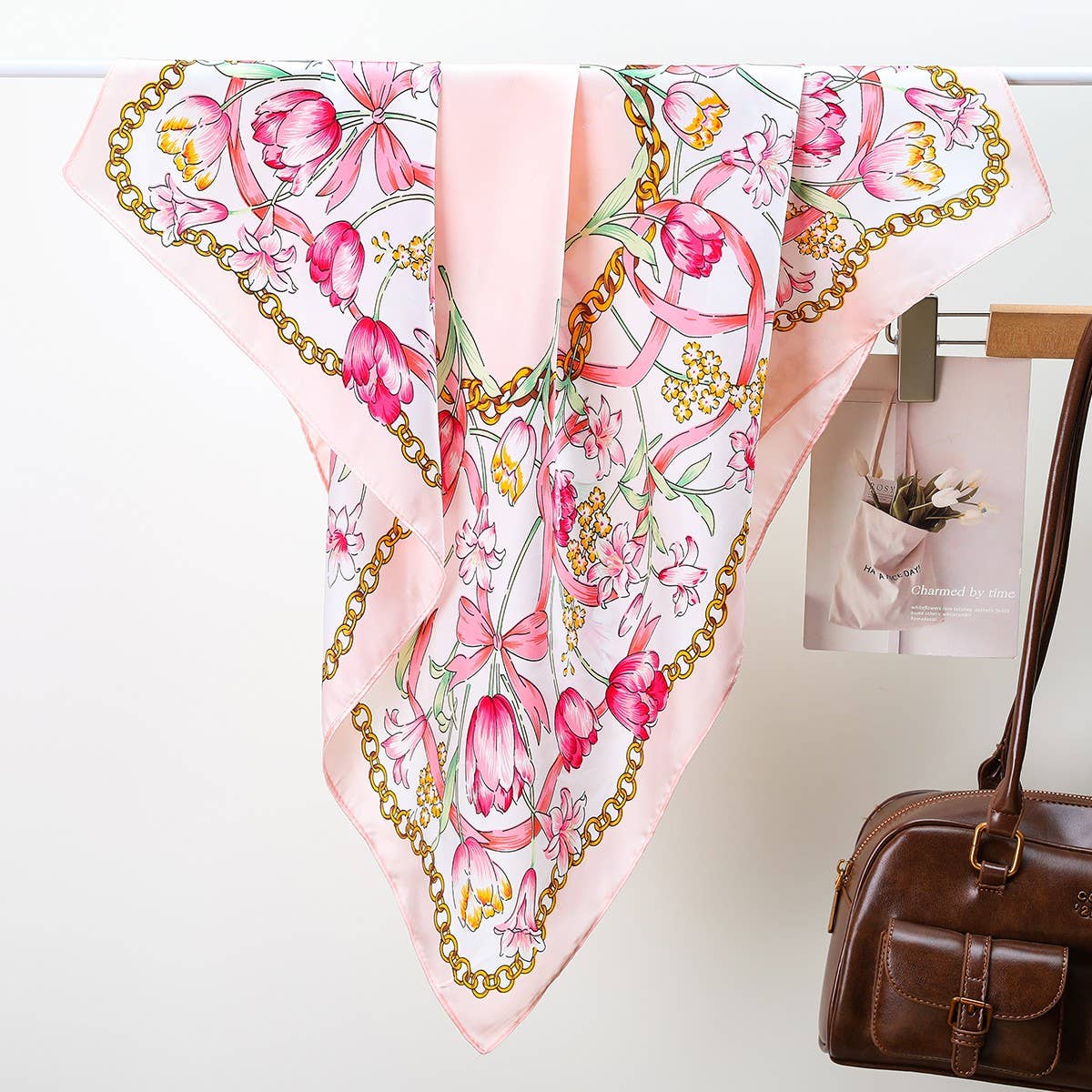 Floral and chain-patterned scarf on a white surface with a brown handbag.