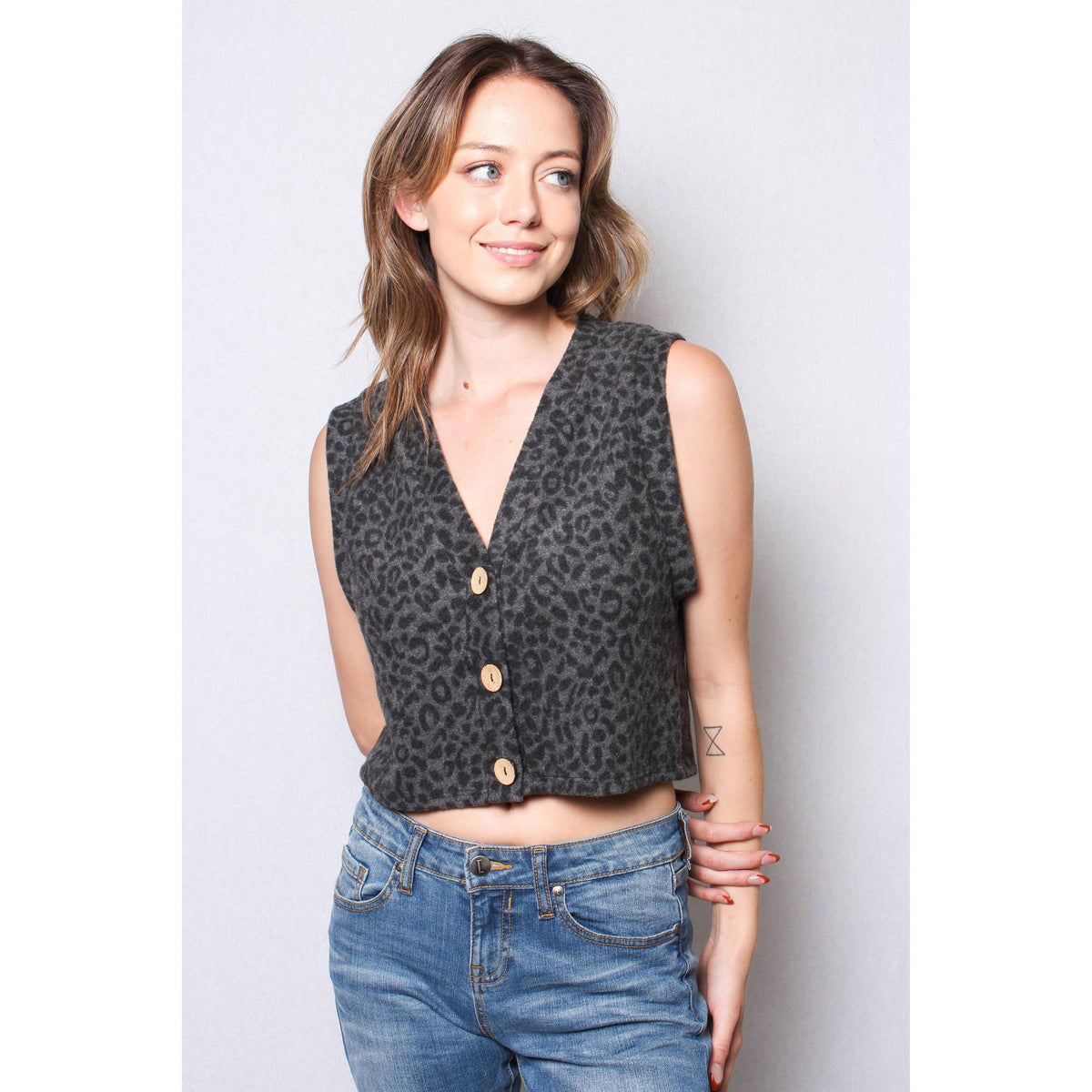 Woman wearing a leopard print vest over a black top with blue jeans against a plain background