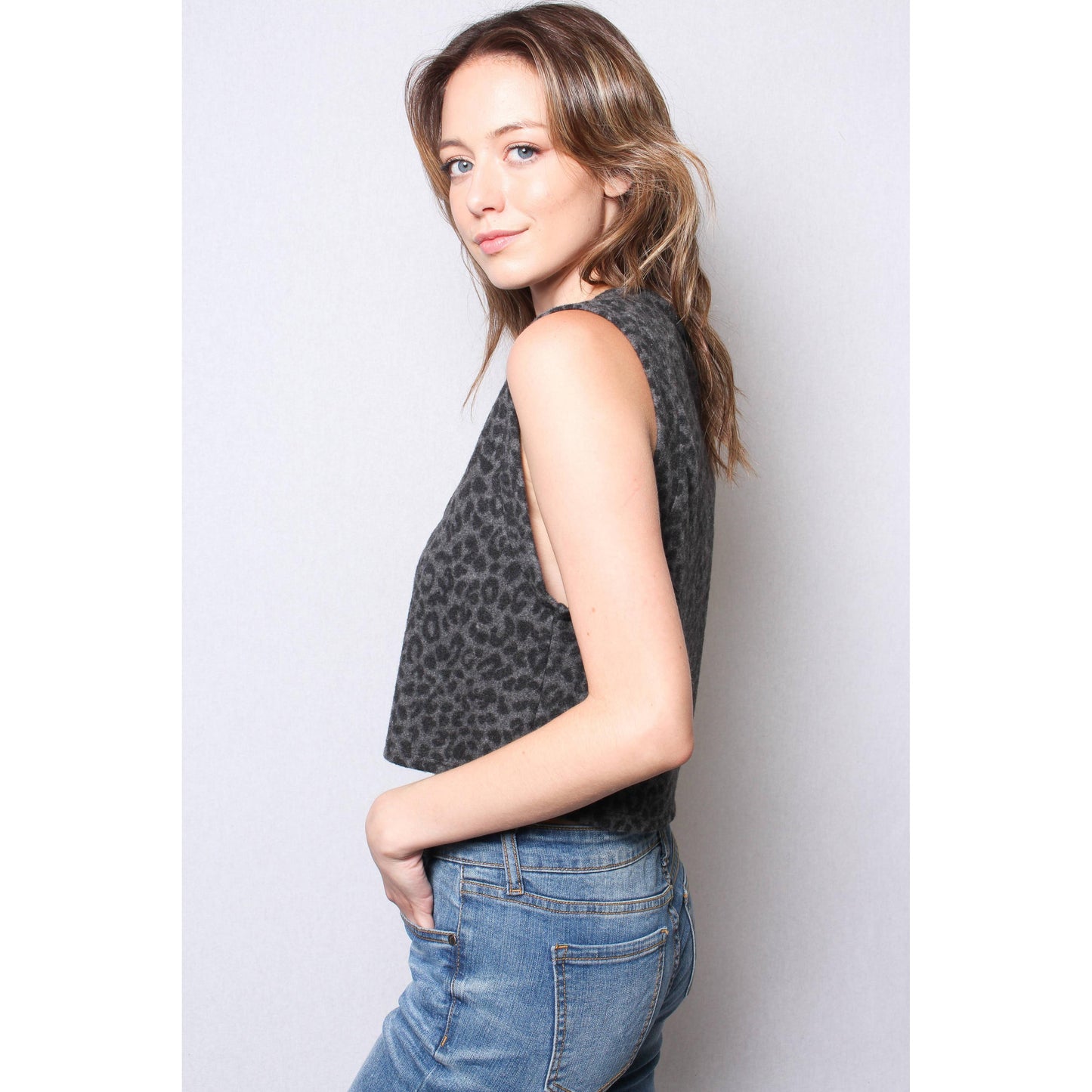 Woman wearing a sleeveless leopard print top and blue jeans against a plain background