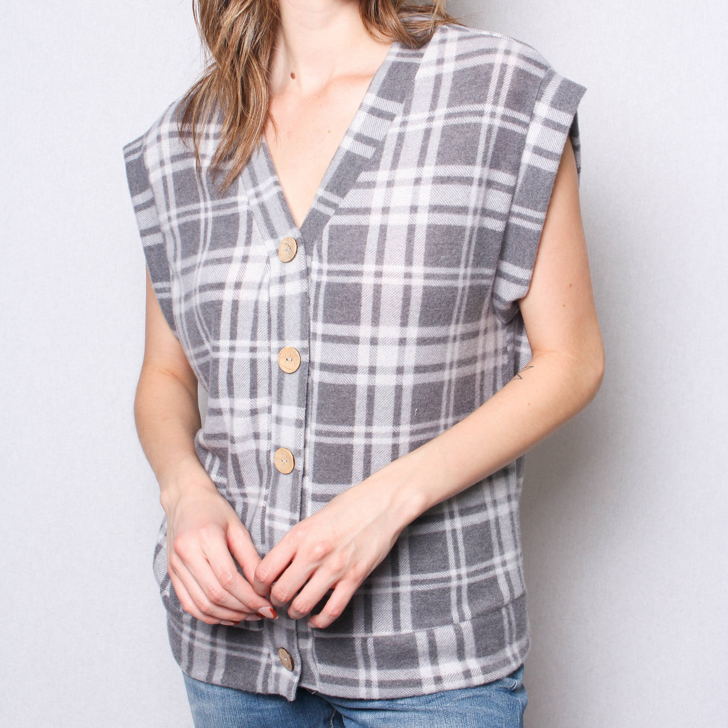 Person wearing a gray plaid sleeveless shirt against a white background