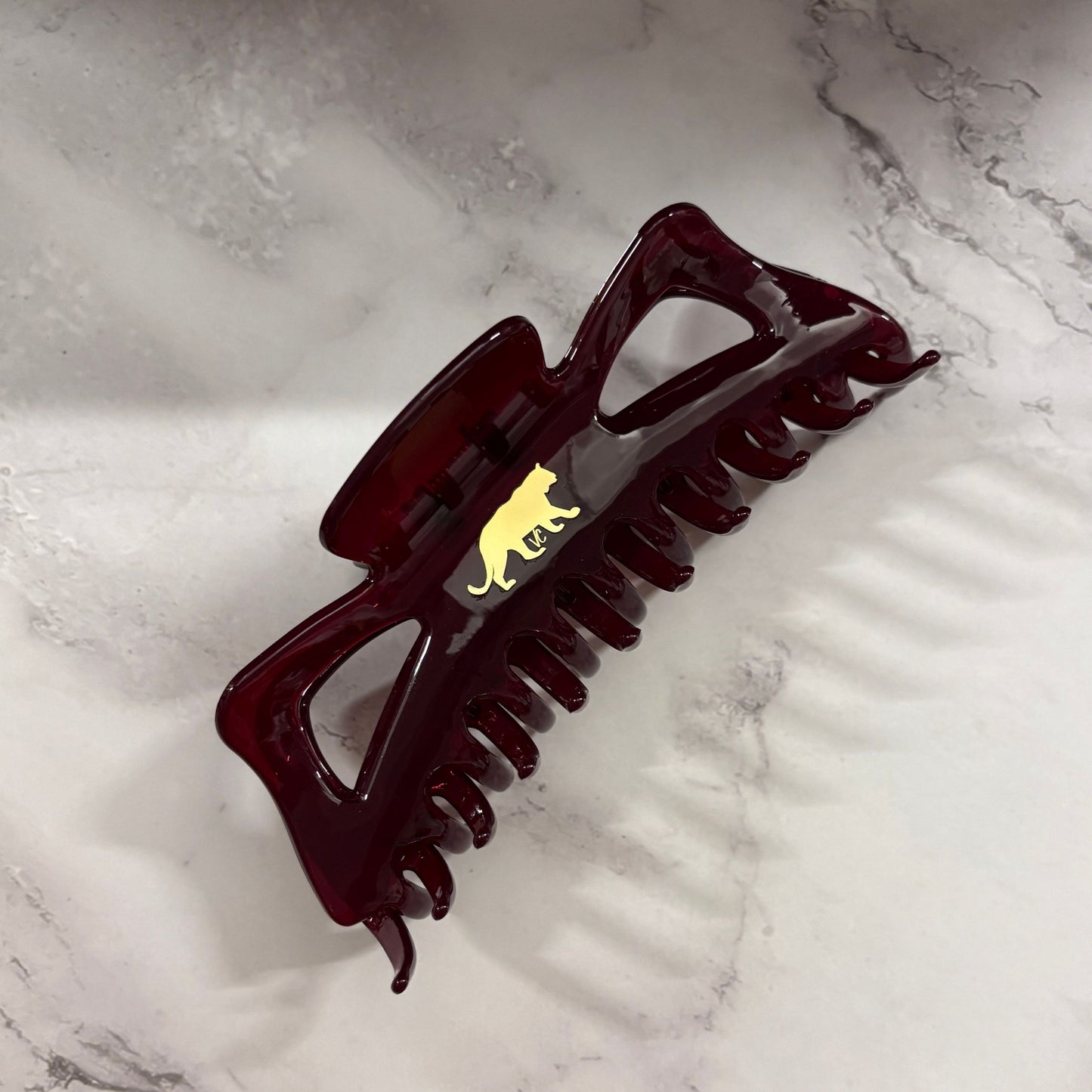 Dark red burgundy hair clip with a gold emblem on a marble surface