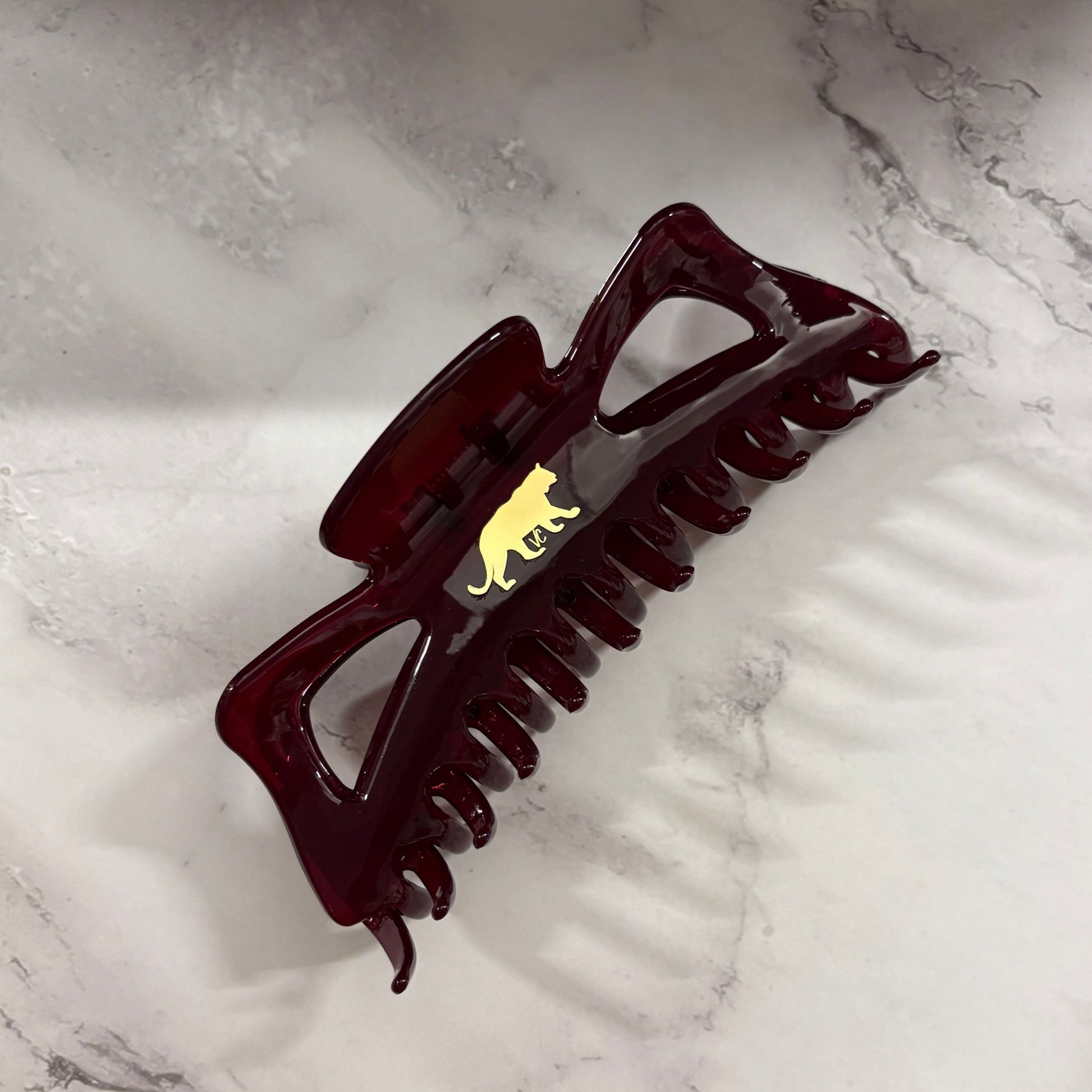 Dark red burgundy hair clip with a gold emblem on a marble surface