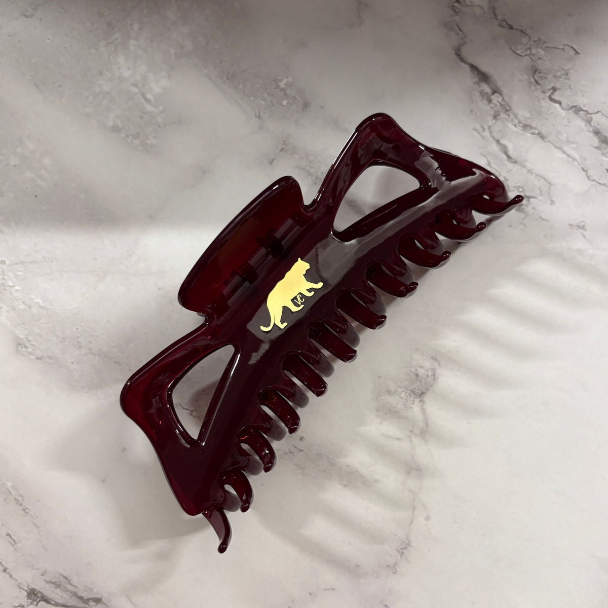 Dark red burgundy hair clip with a gold emblem on a marble surface