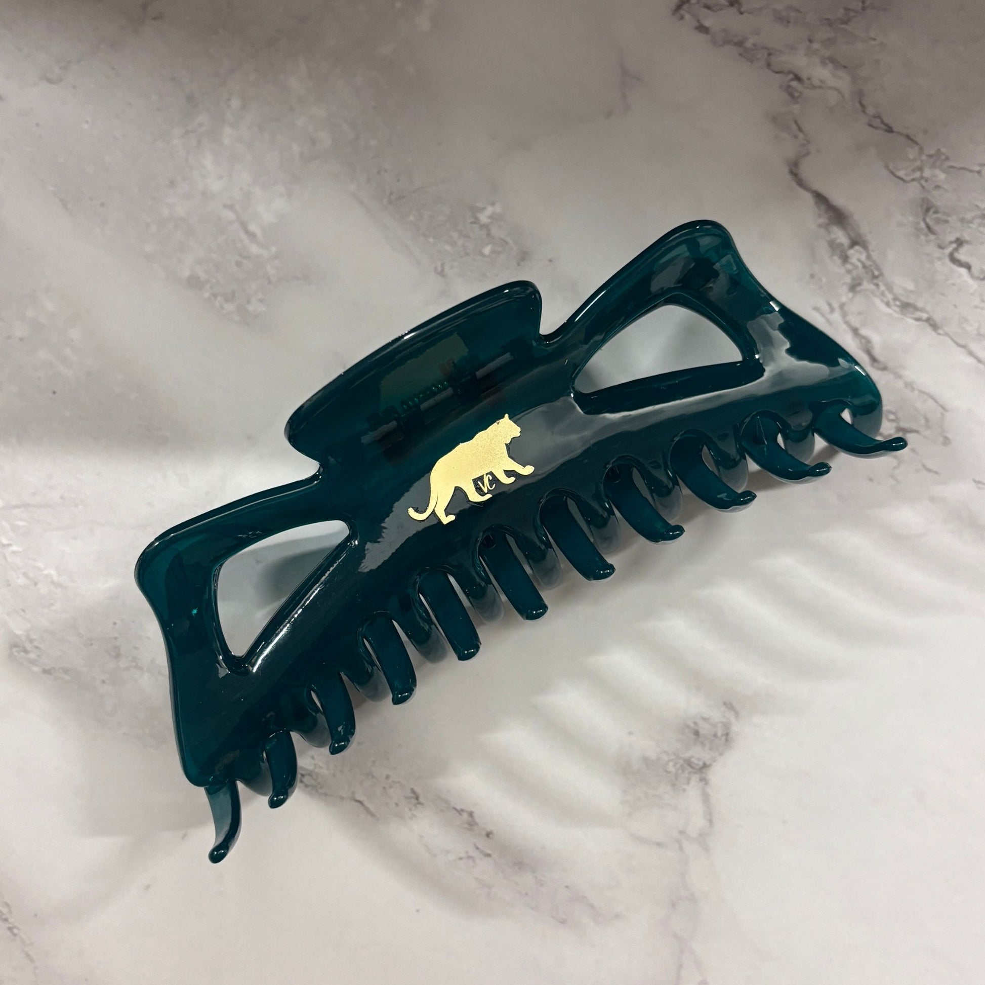 Dark green hair clip with a gold panther emblem on a marble surface