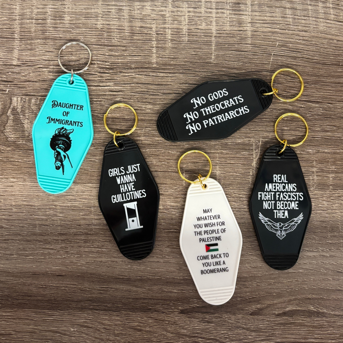 Five keychains with political-themed text and graphics on a wooden surface