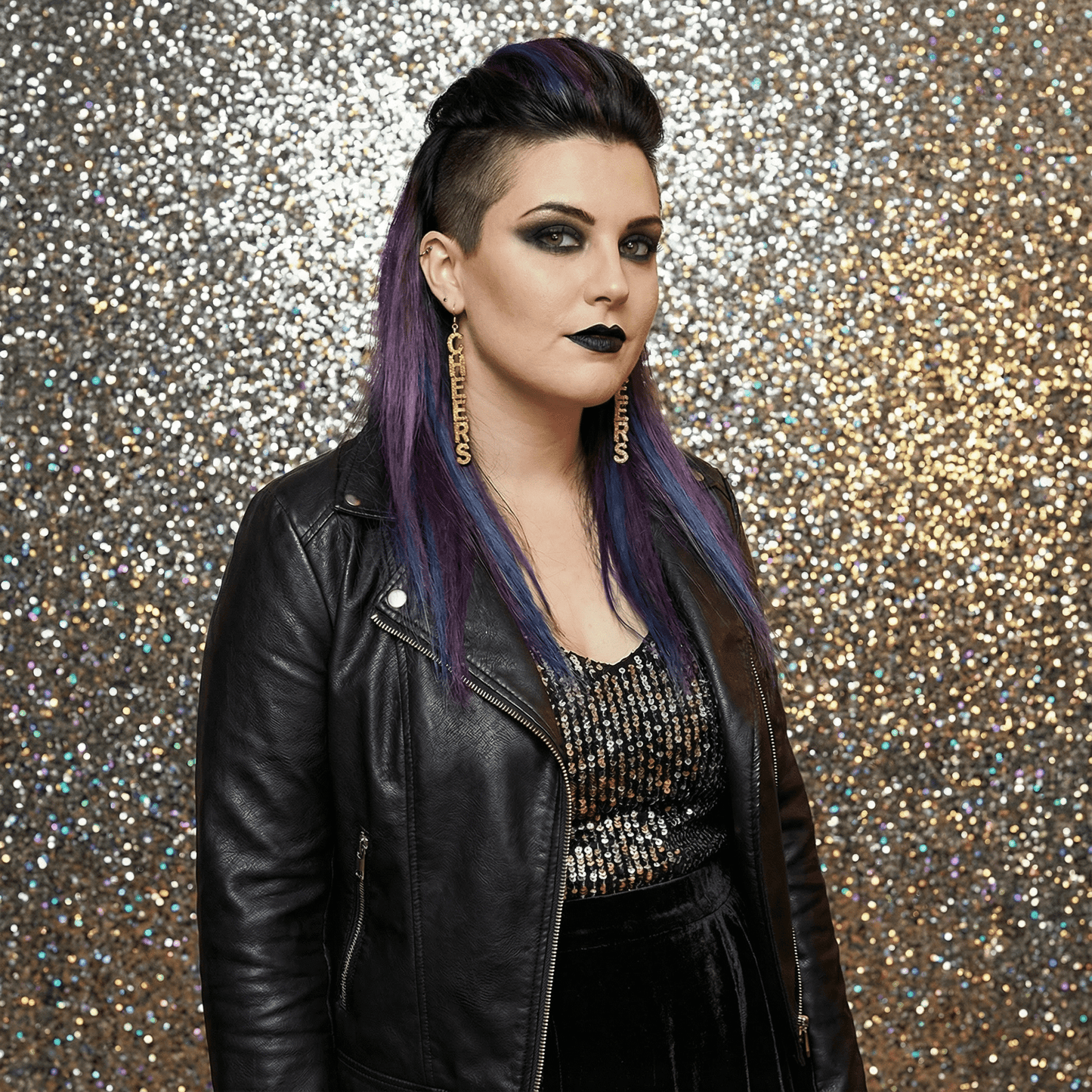 Person with purple hair and black leather jacket against a glittery background