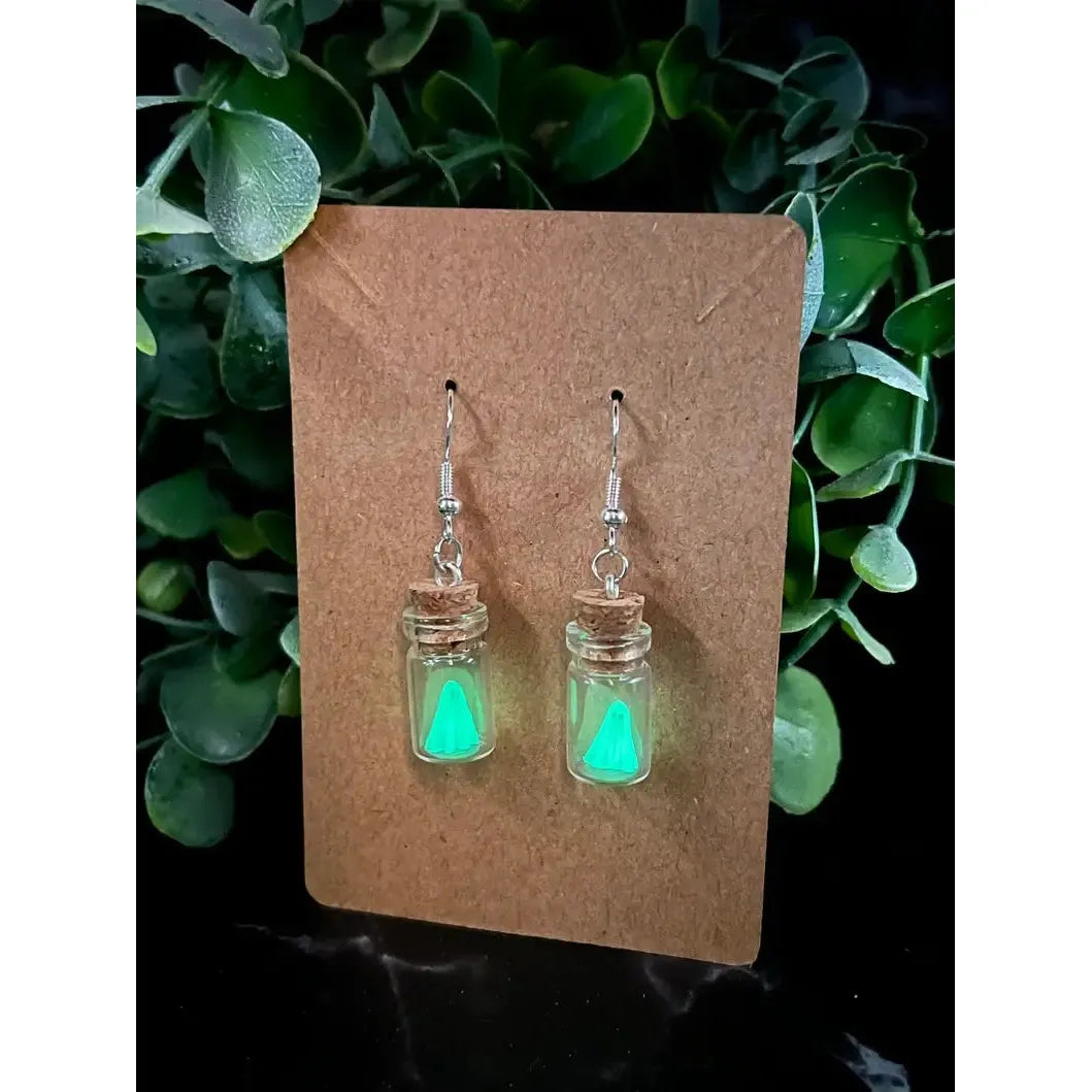 Glowing green jar earrings on a brown card with green leaves in the background