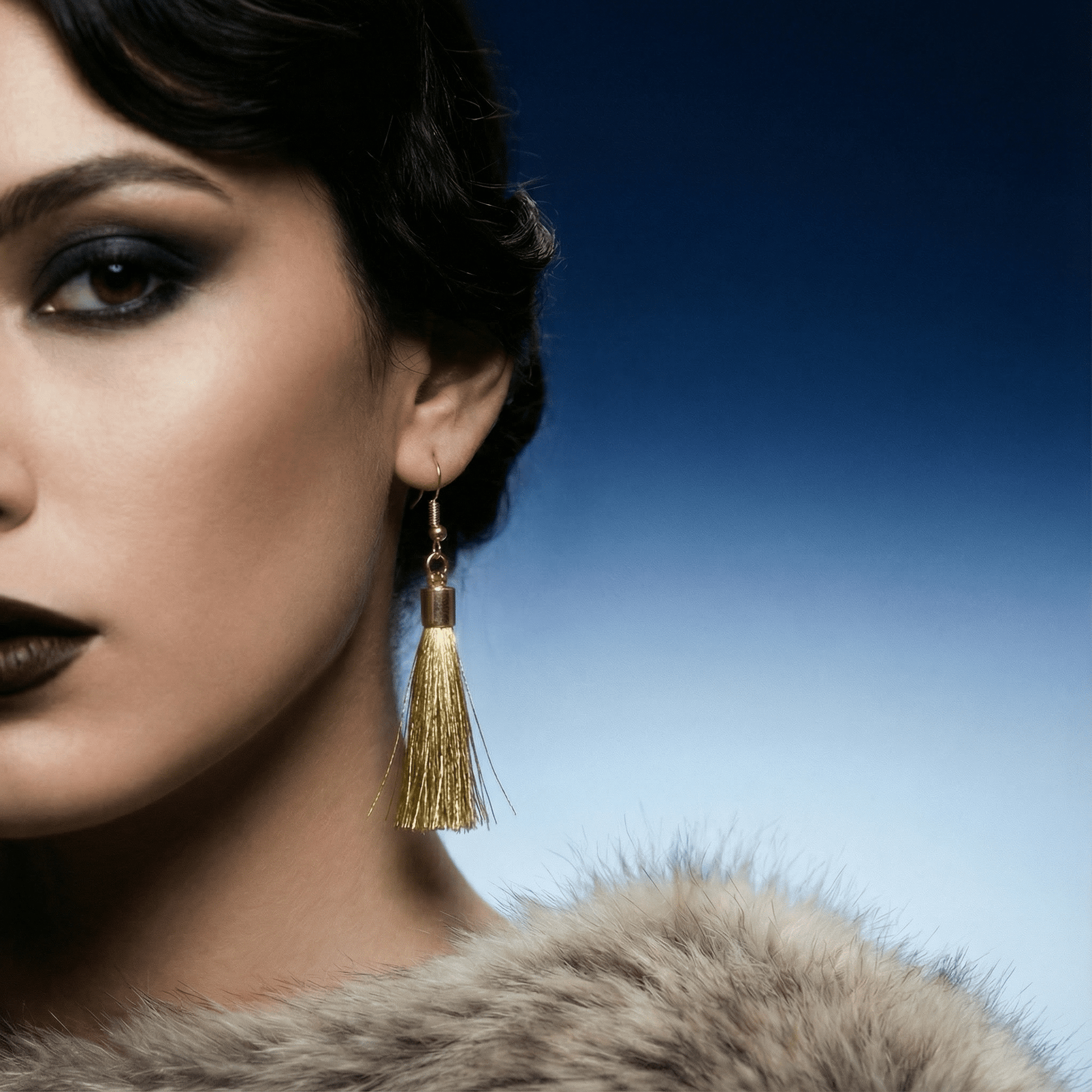 Close-up of a woman wearing gold tassel earrings with a blue gradient background