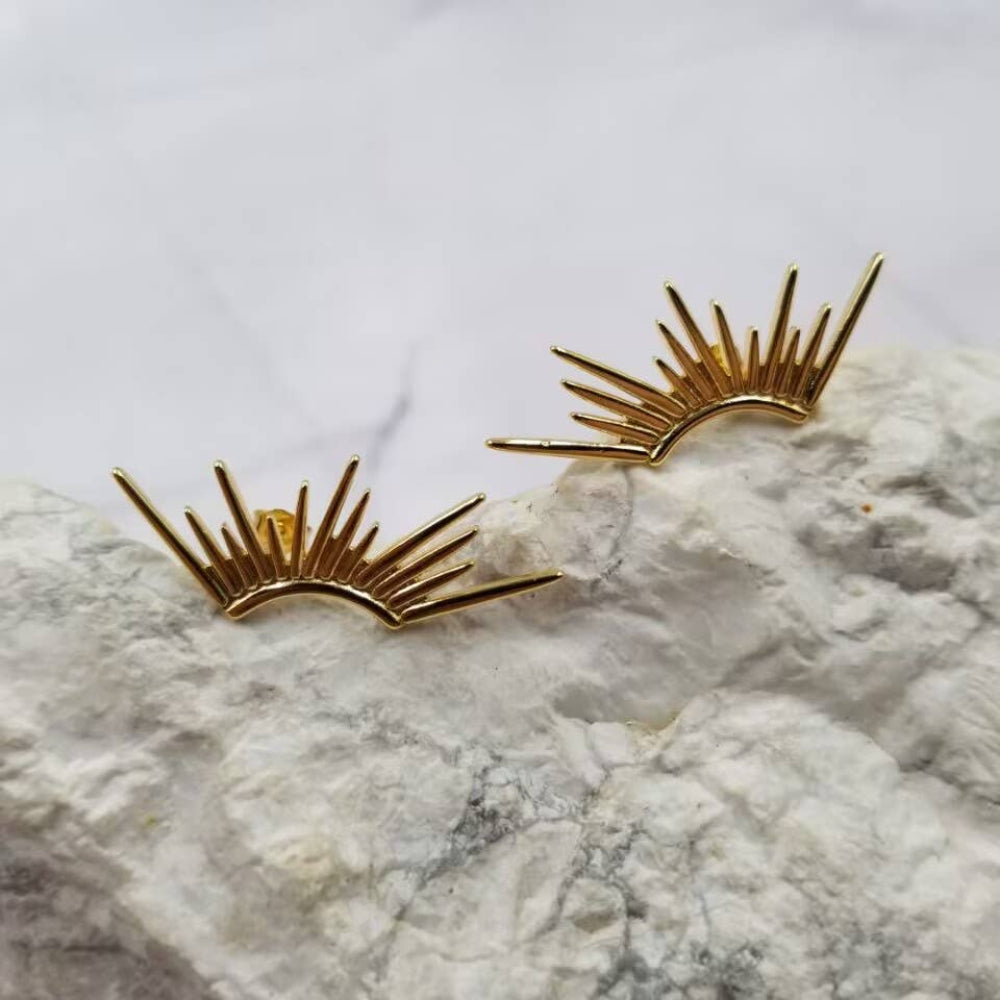 Gold sunburst earrings on a marble surface