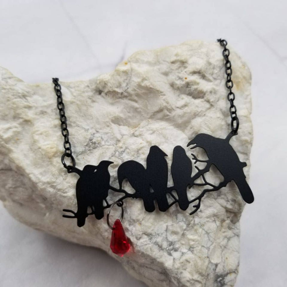 Necklace with black raven bird silhouettes and a red pendant on a white stone background