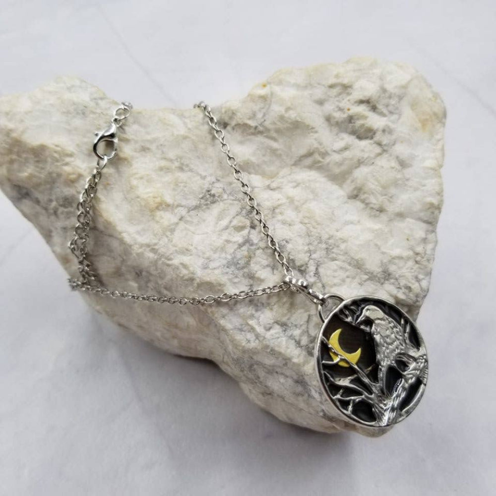 Silver necklace with a pendant featuring a bird and moon design, placed on a textured stone surface.