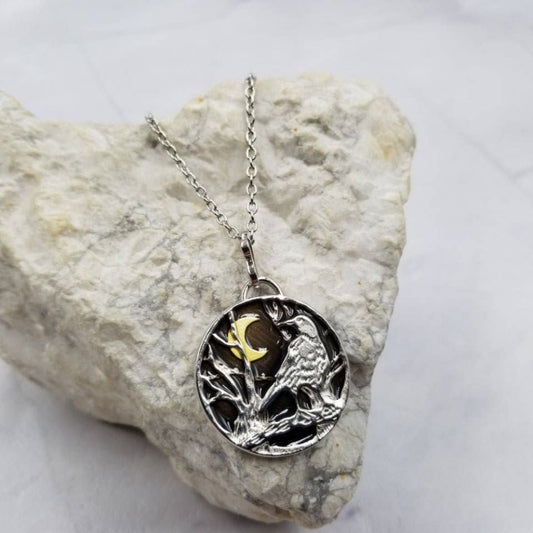 Silver necklace with a pendant featuring a bird and moon design, placed on a textured stone surface.