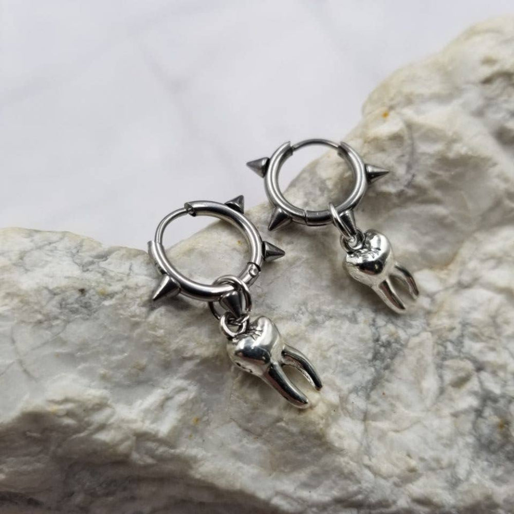 Pair of silver hoop earrings with spike details on a stone surface