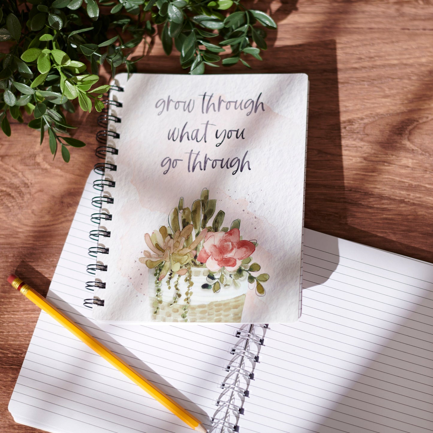 Open notebook with motivational quote and floral illustration on a wooden surface with a plant.