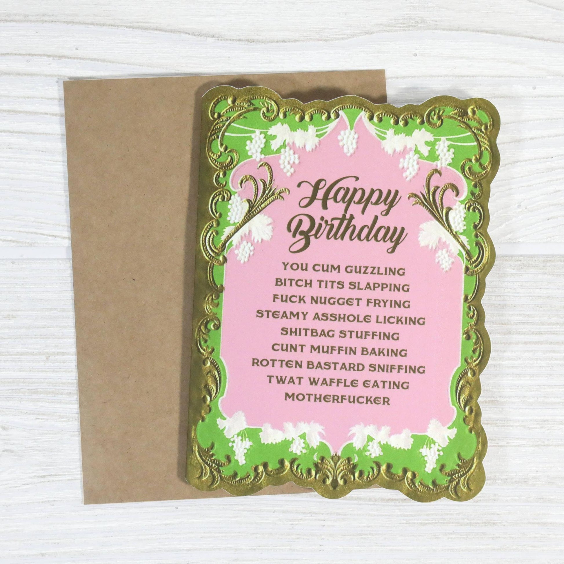 Birthday card with offensive language on a pink background with gold and green decorative elements.