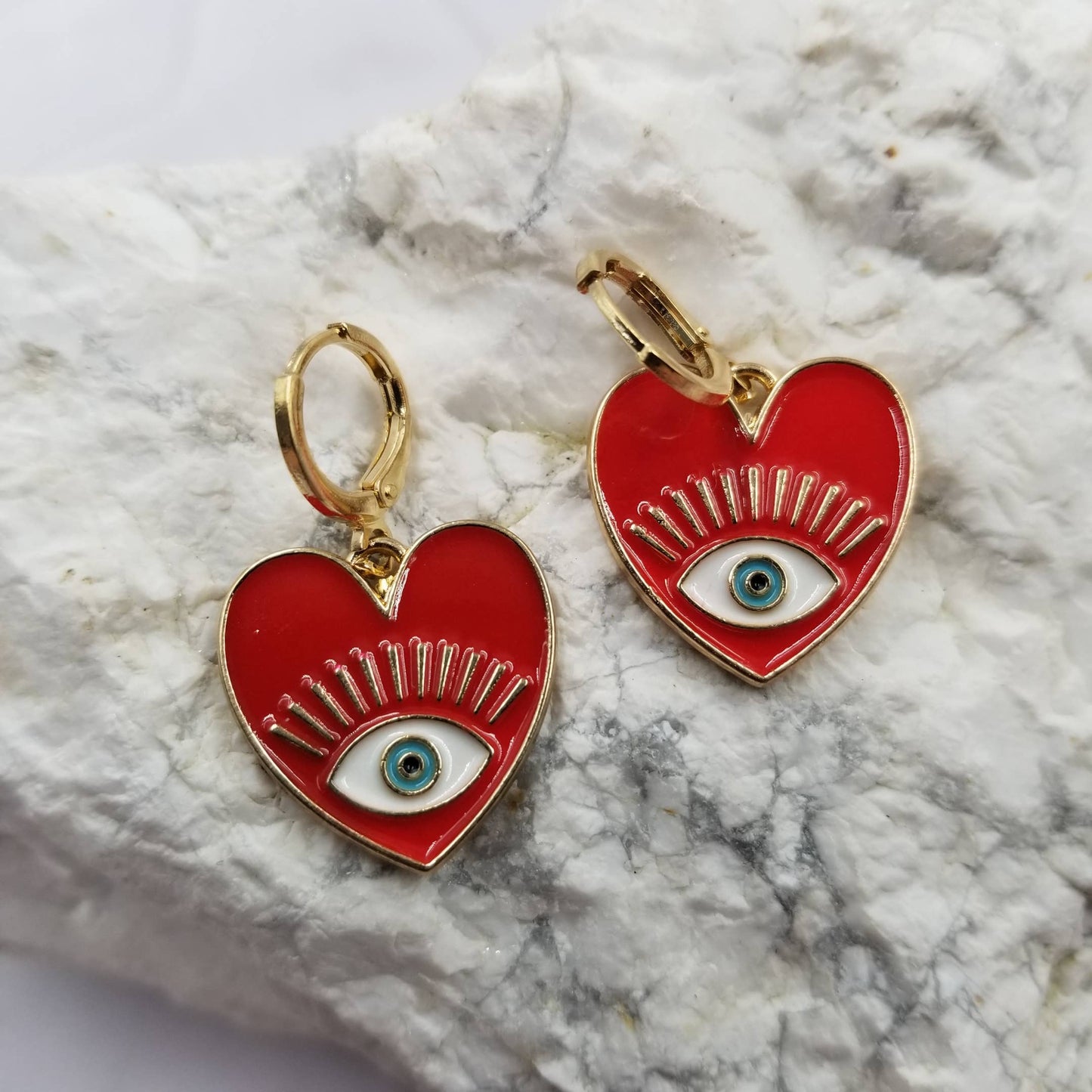 Red heart-shaped earrings with eye design on a marble surface