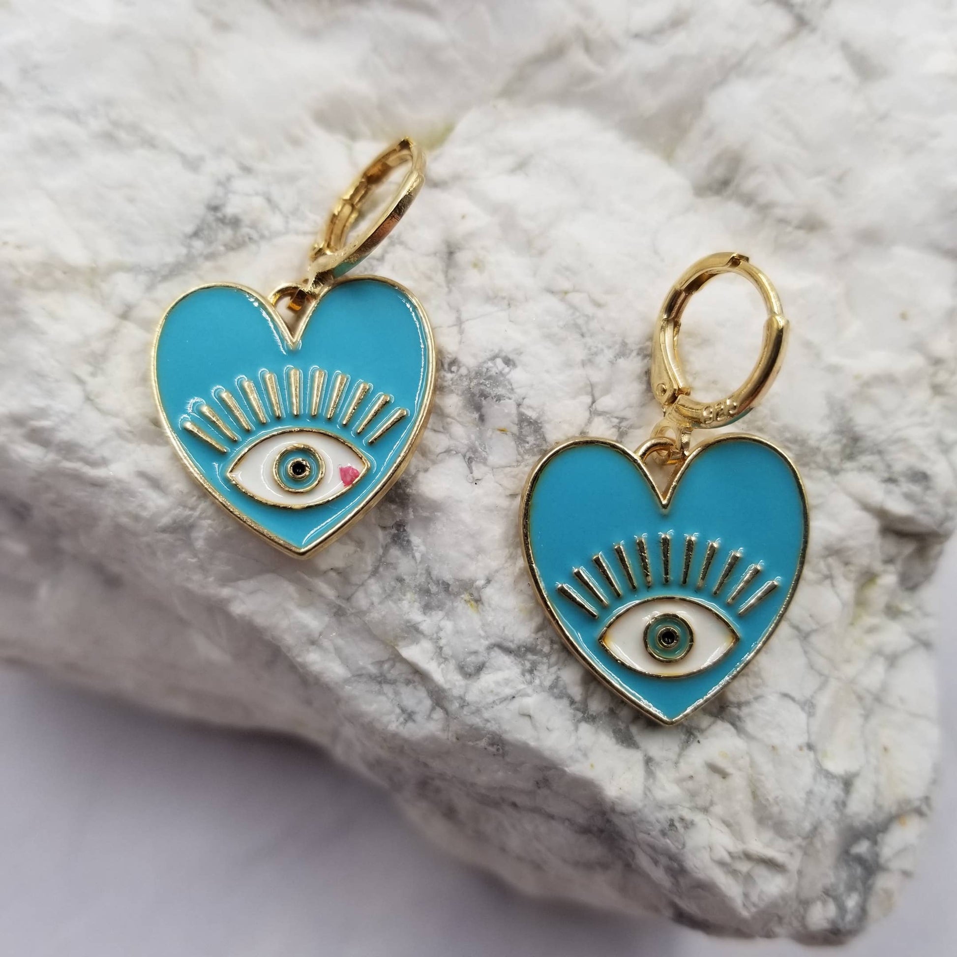 Light blue heart-shaped earrings with eye design on a textured stone surface