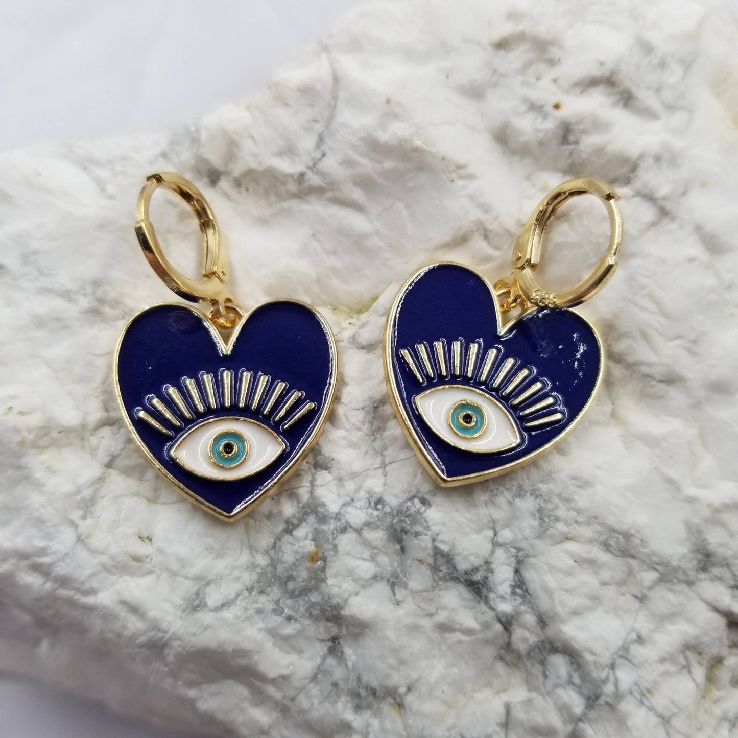 Dark blue heart-shaped earrings with eye design on a marble surface