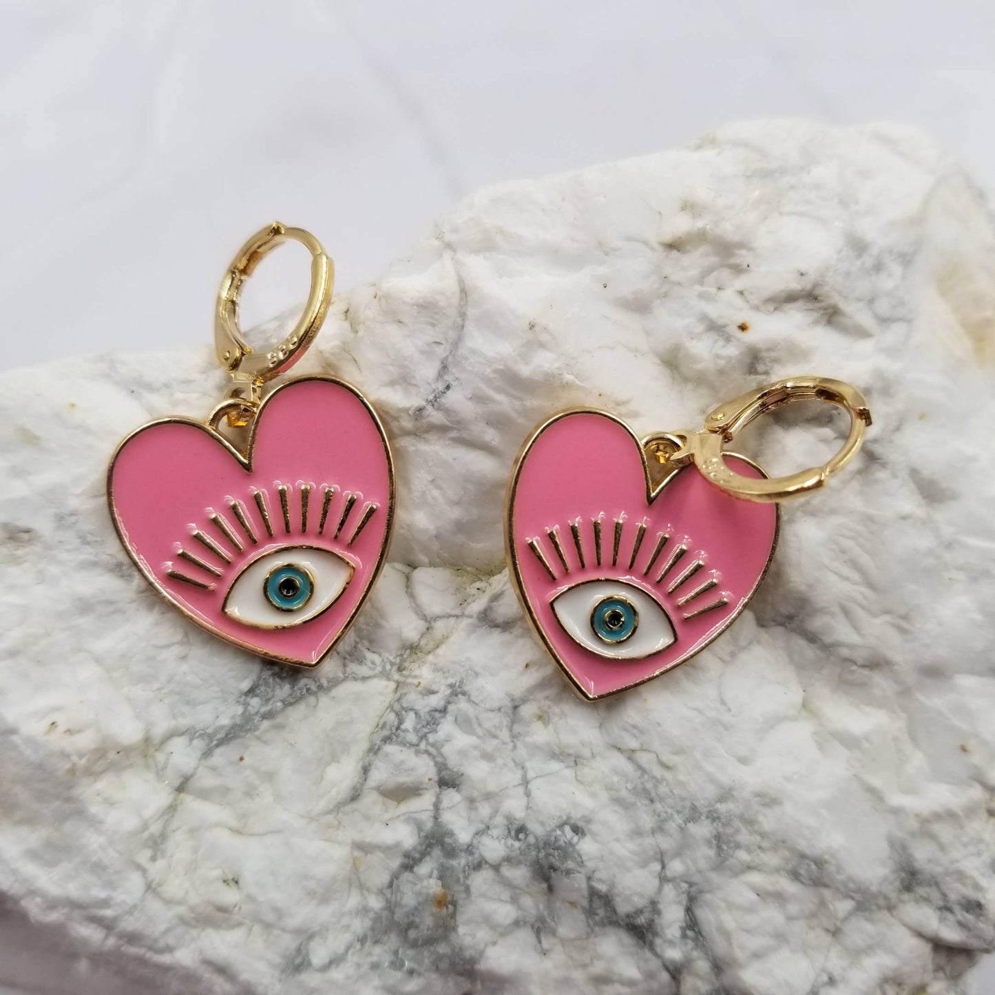 Pink heart-shaped earrings with eye design on a marble surface