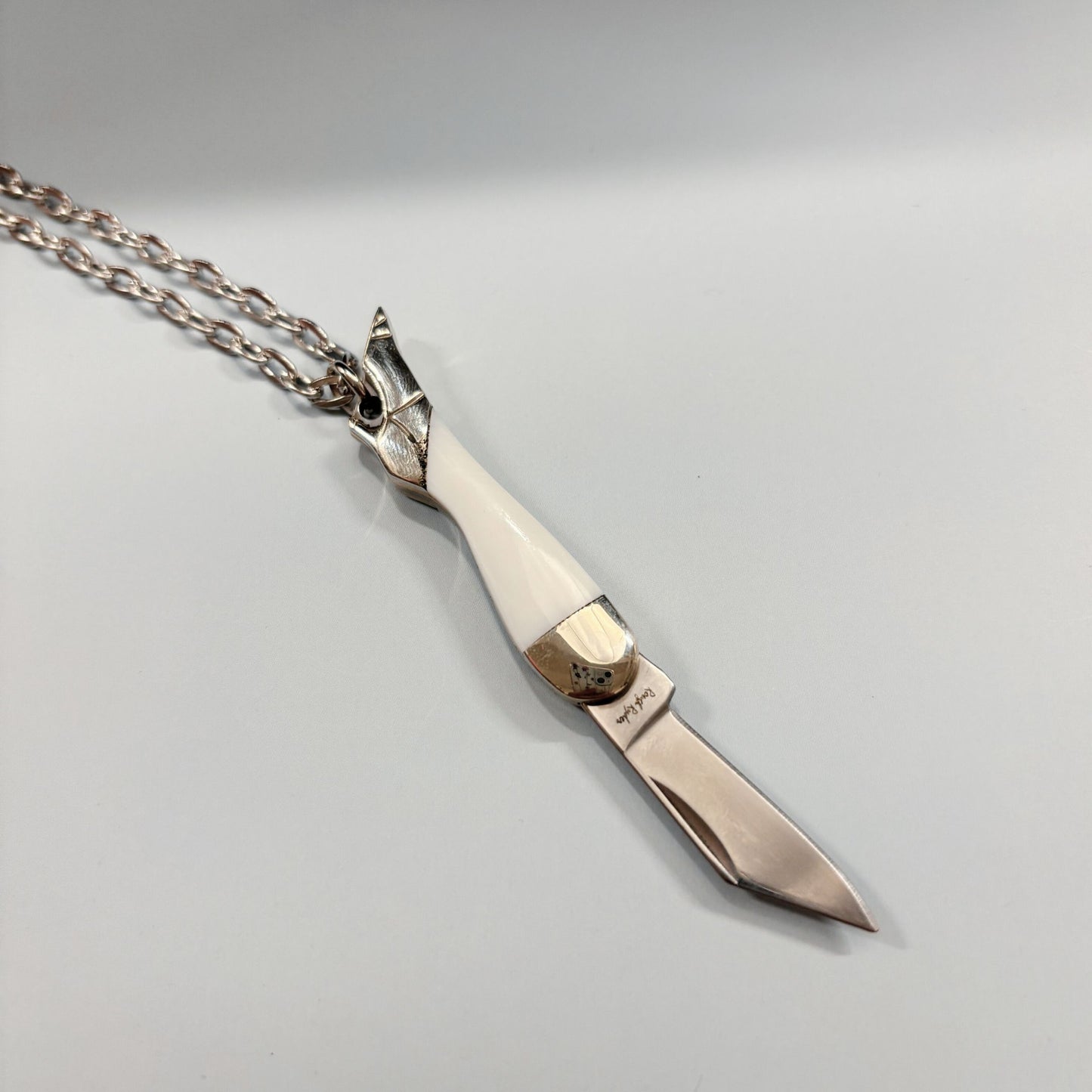 Silver knife-shaped pendant on a chain against a gray background