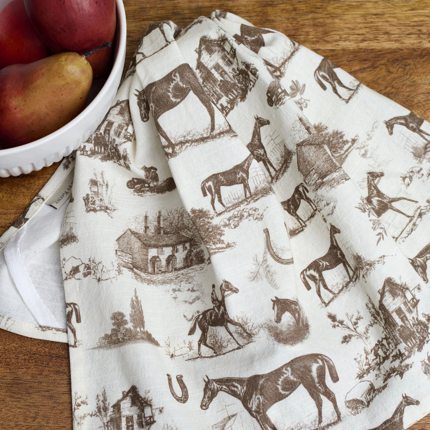 Dish towel with vintage-style horse and farm scene pattern on a wooden surface with pears.