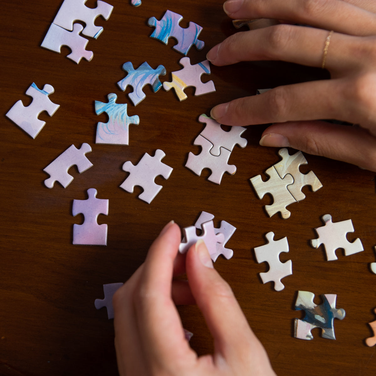 Hands arranging puzzle pieces on a wooden surface