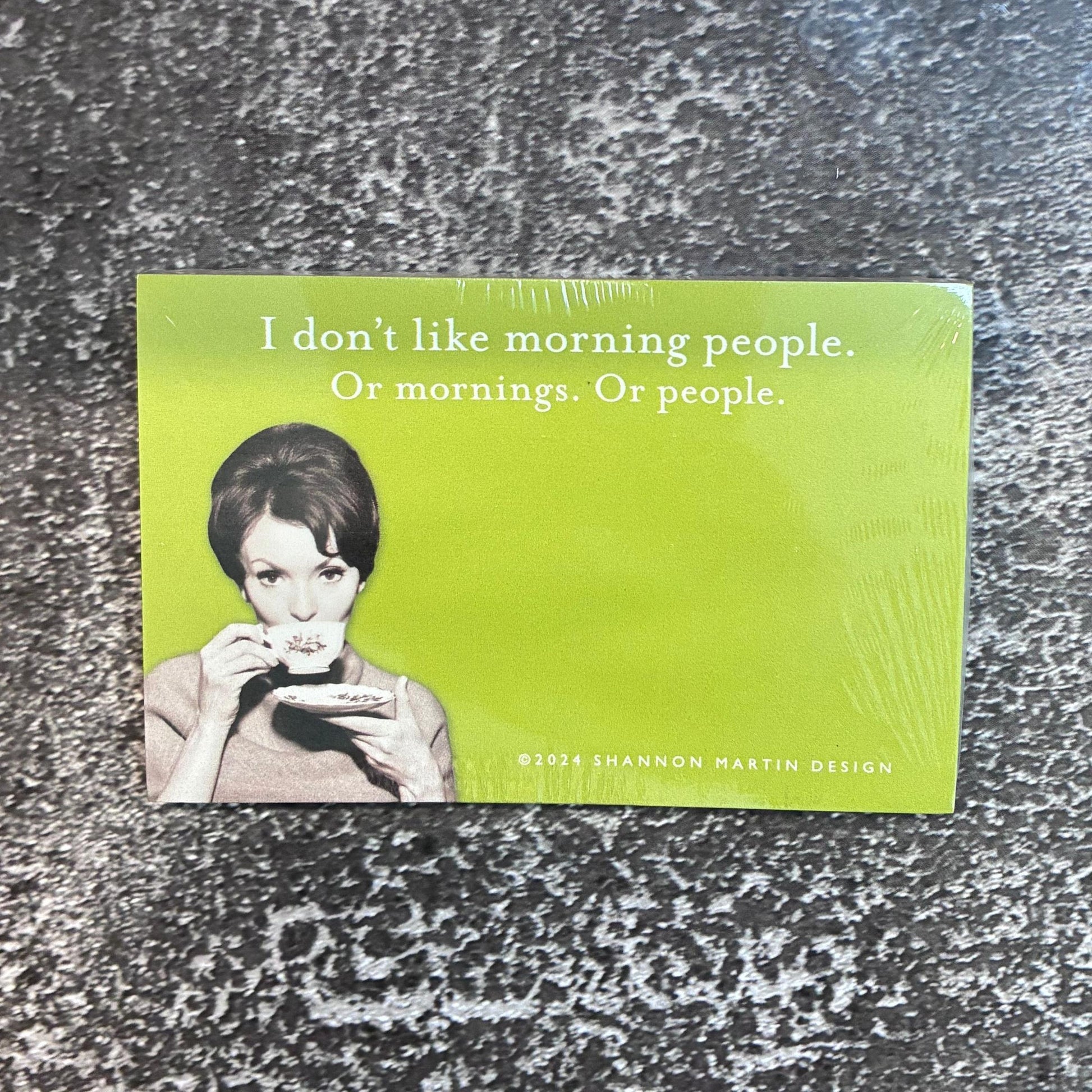 Green sticky notepad with a woman drinking coffee and text on a textured surface