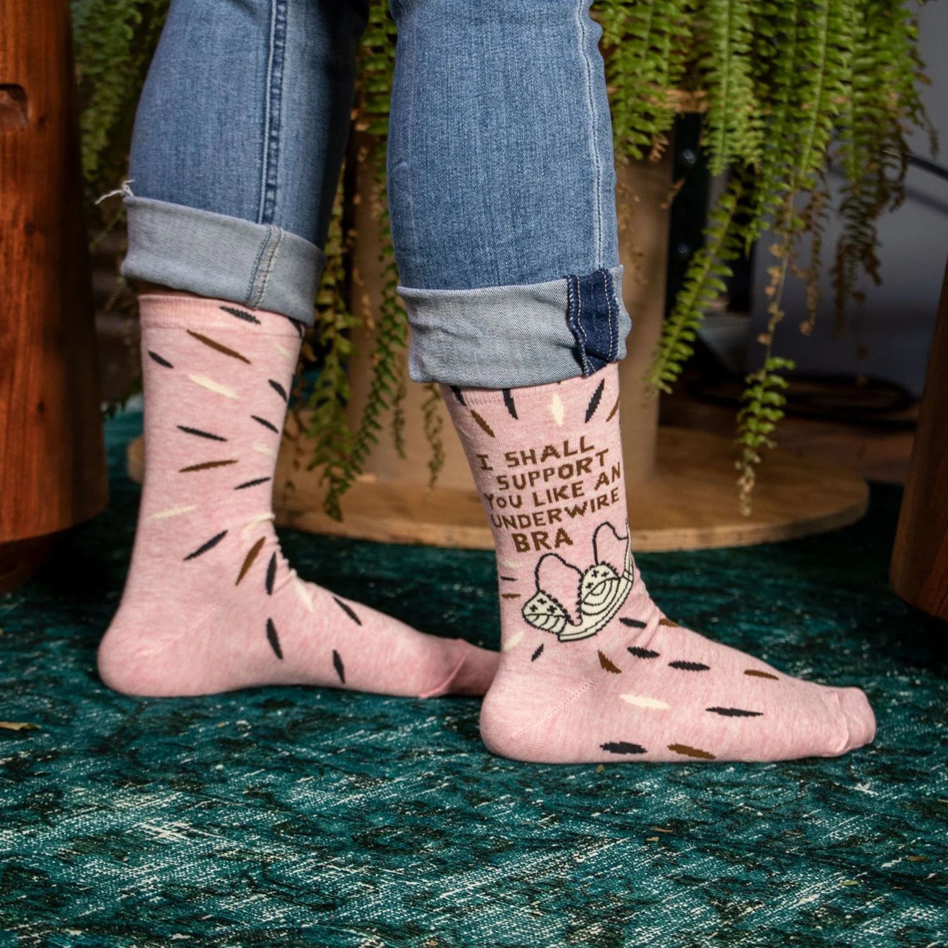 Person wearing pink socks with text and graphics, standing on a green surface with plants in the background.