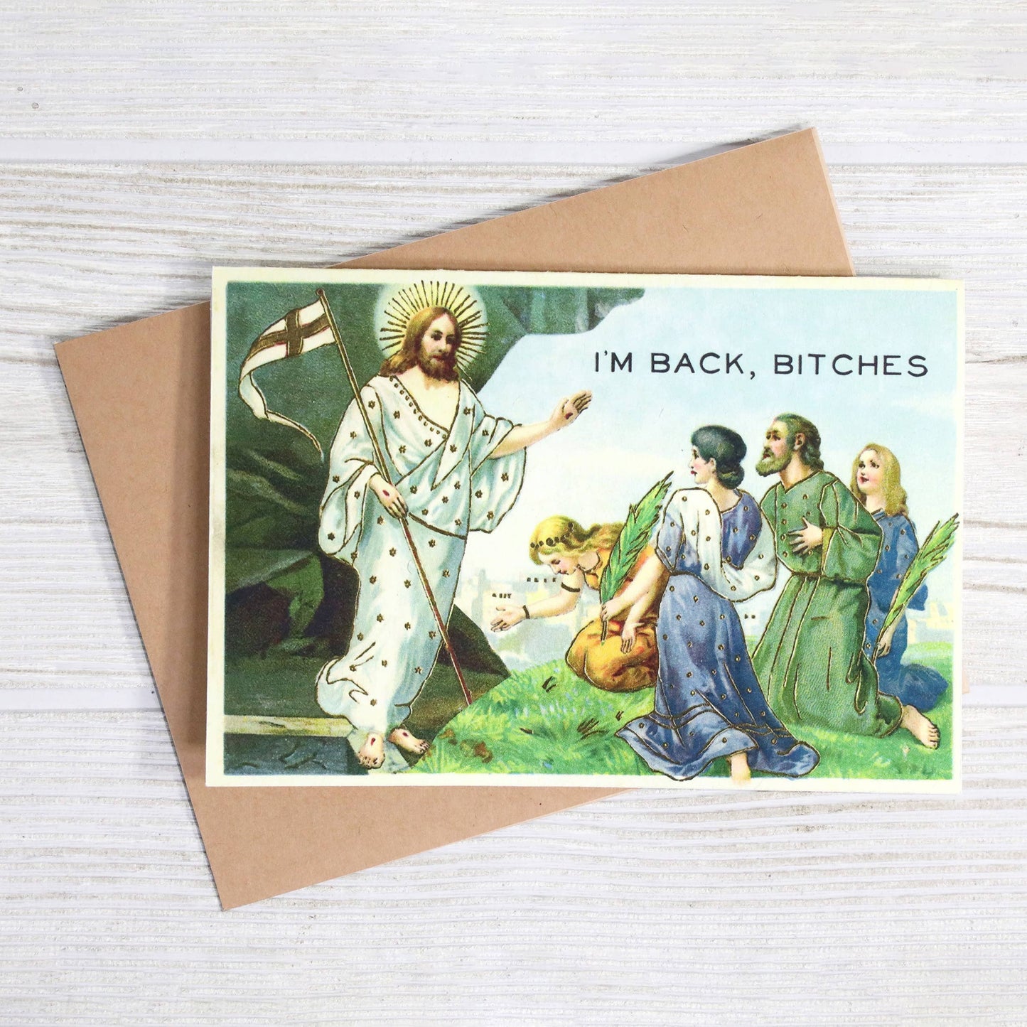 Card with religious illustration and text 'I'm Back, Bitches' on a wooden surface