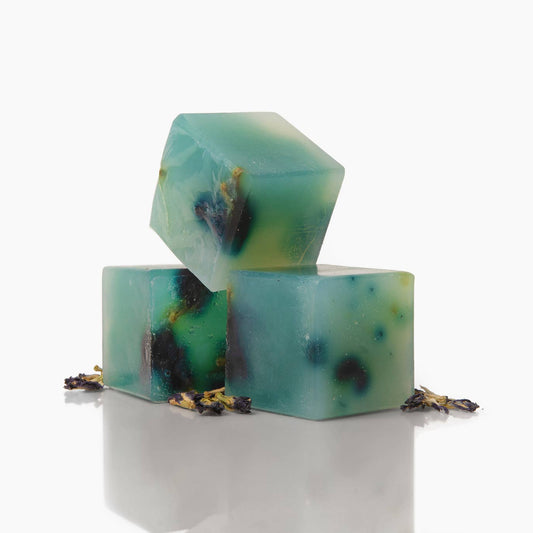 Three cube green soaps with specks on a white background