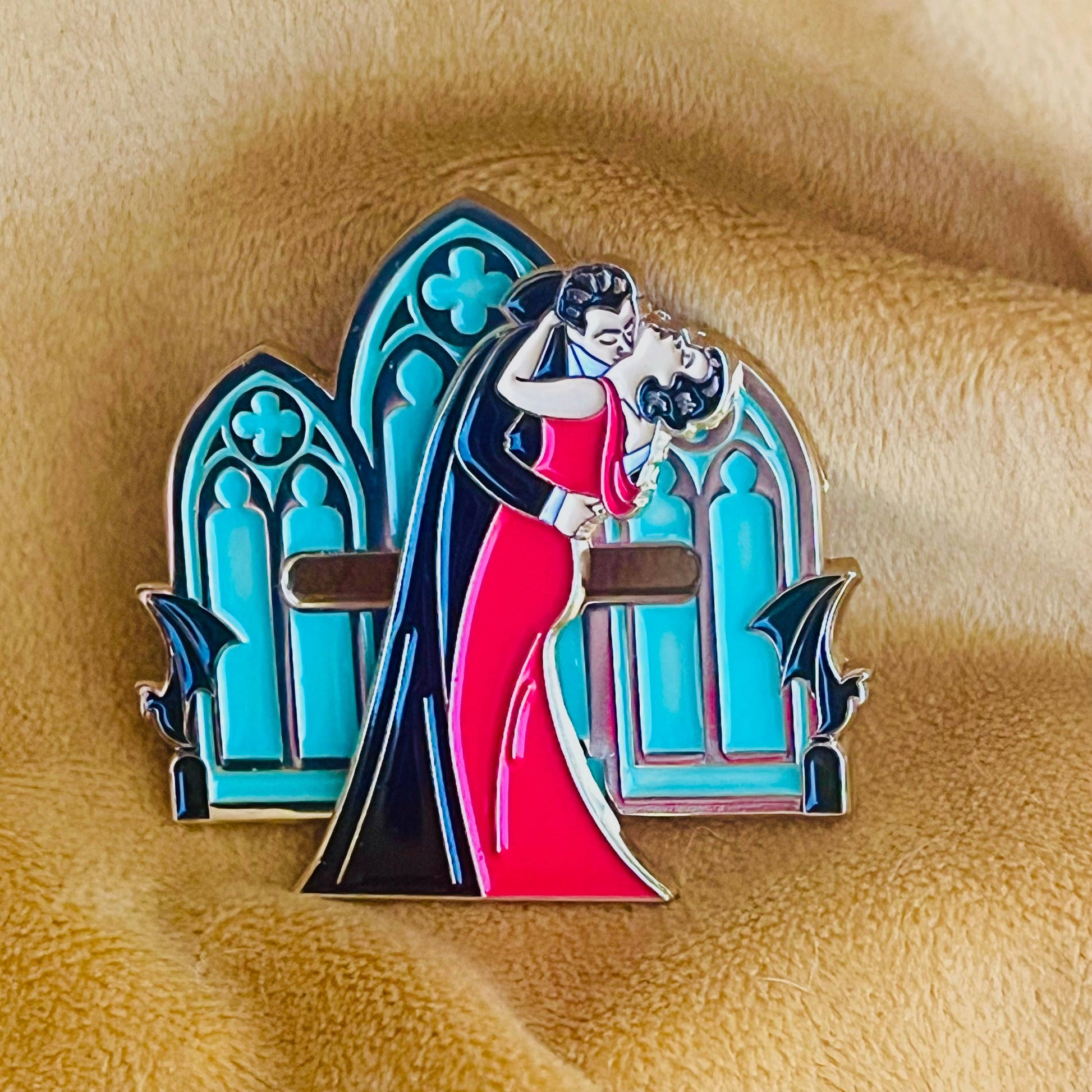 Enamel pin with a design of a woman in a red dress being lifted by a man, set against a blue archway