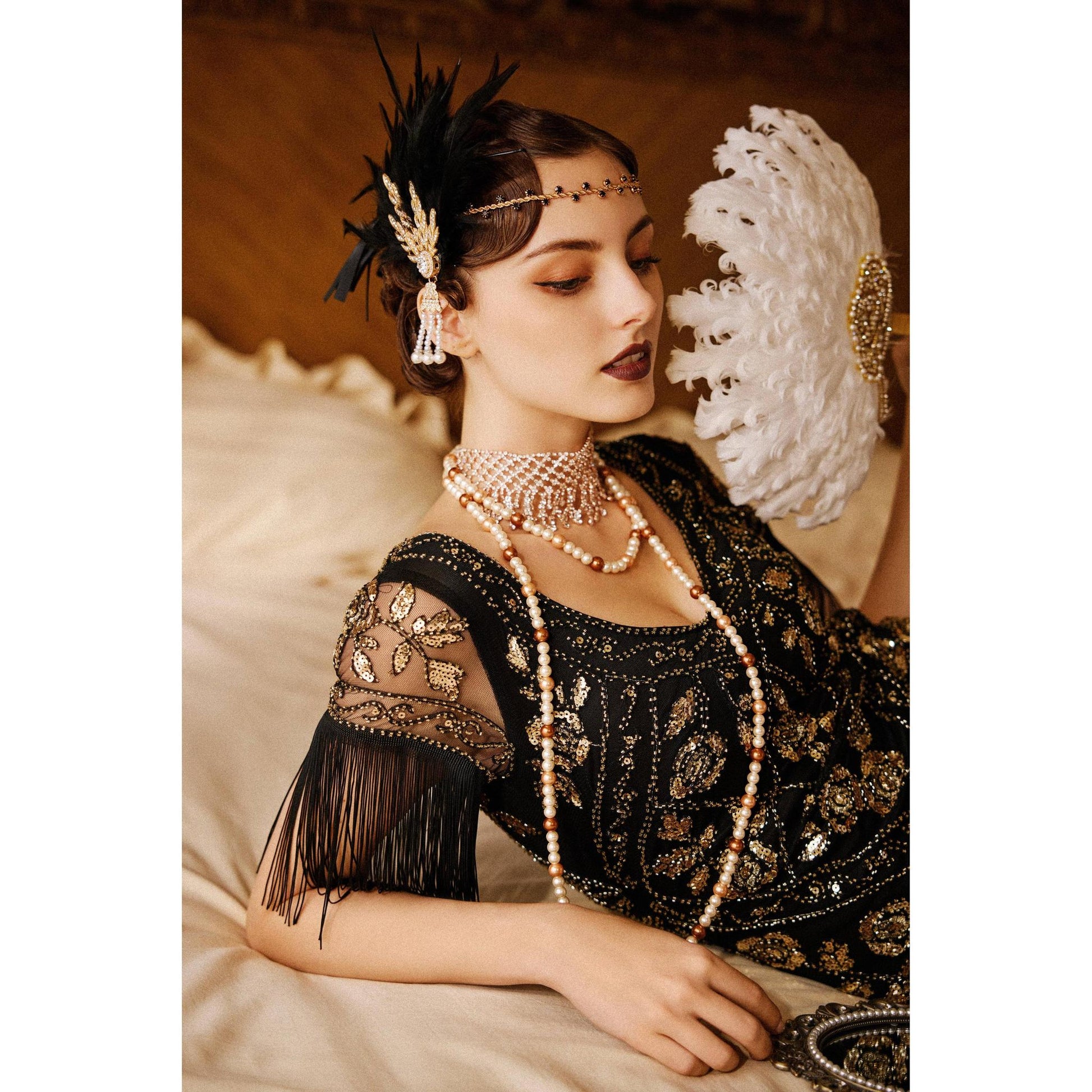 Woman in a black dress with gold embellishments and jewelry, holding a decorative fan.