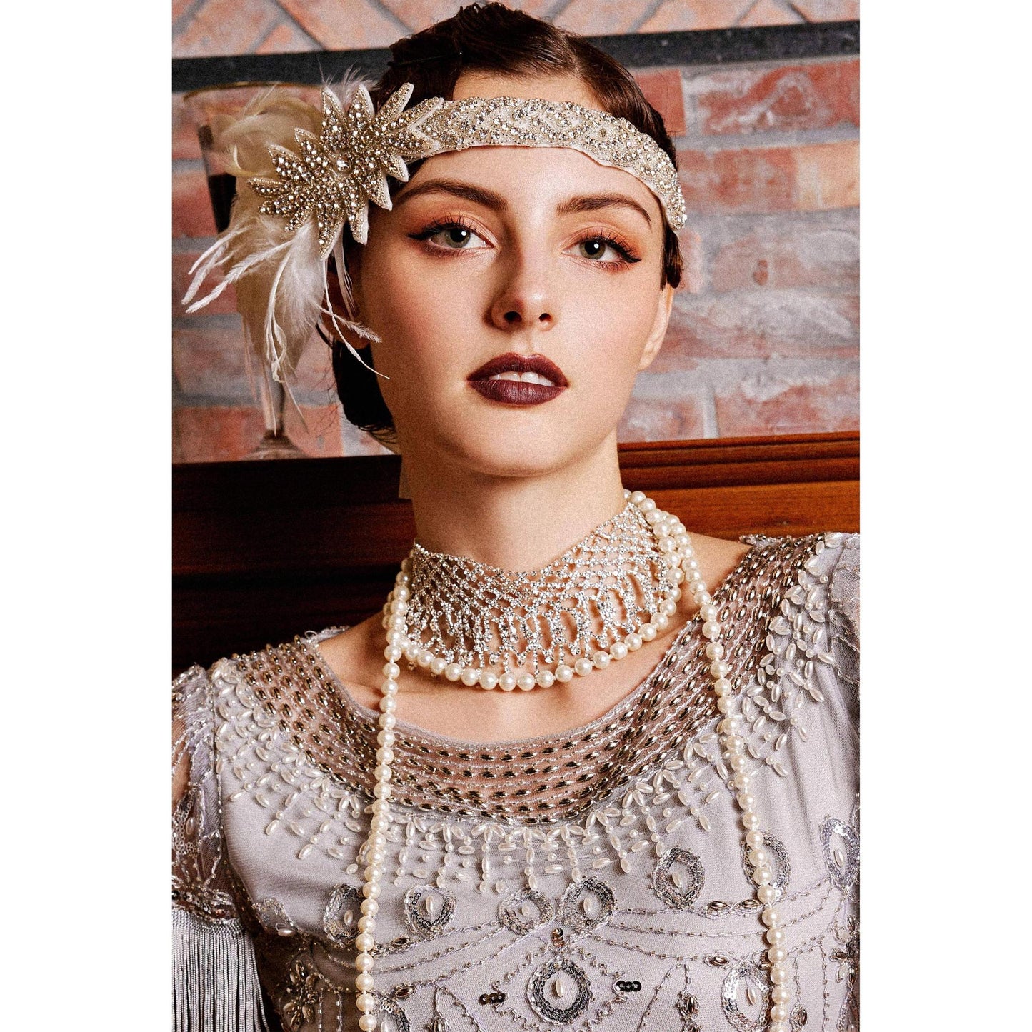 Woman wearing a vintage-style headband and pearl necklace against a brick wall.
