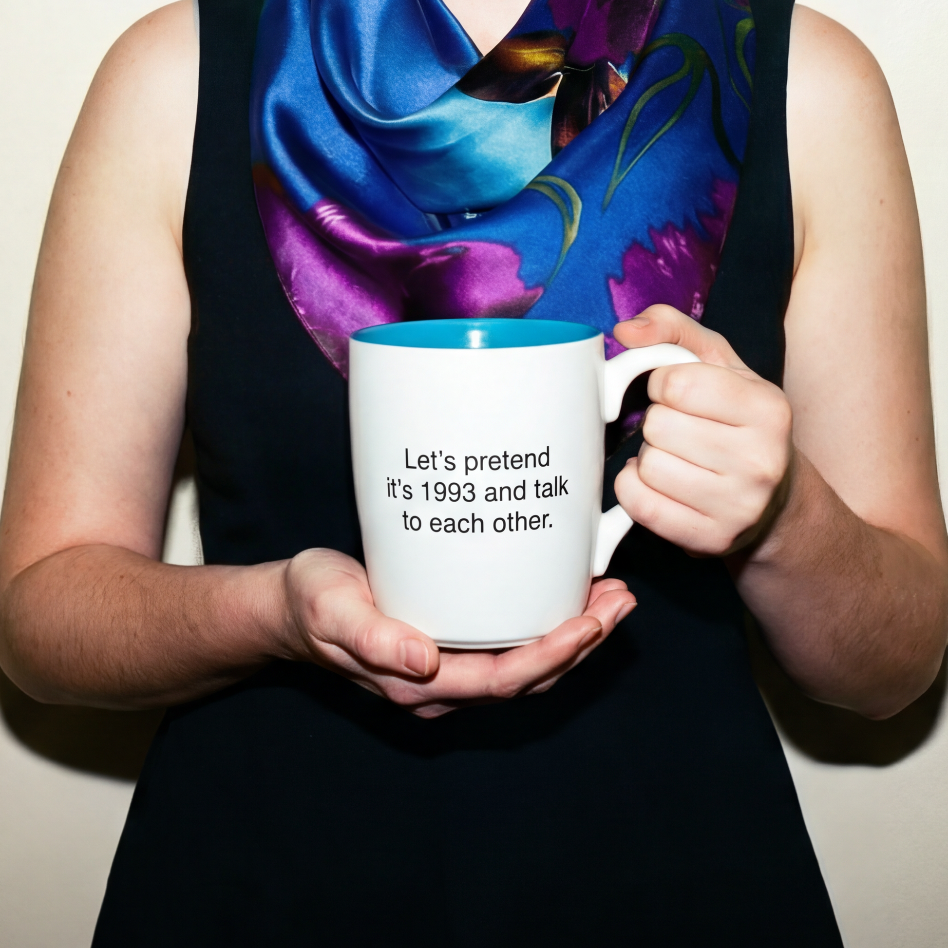 Woman wearing a colorful scarf and holding a mug with text against a plain background