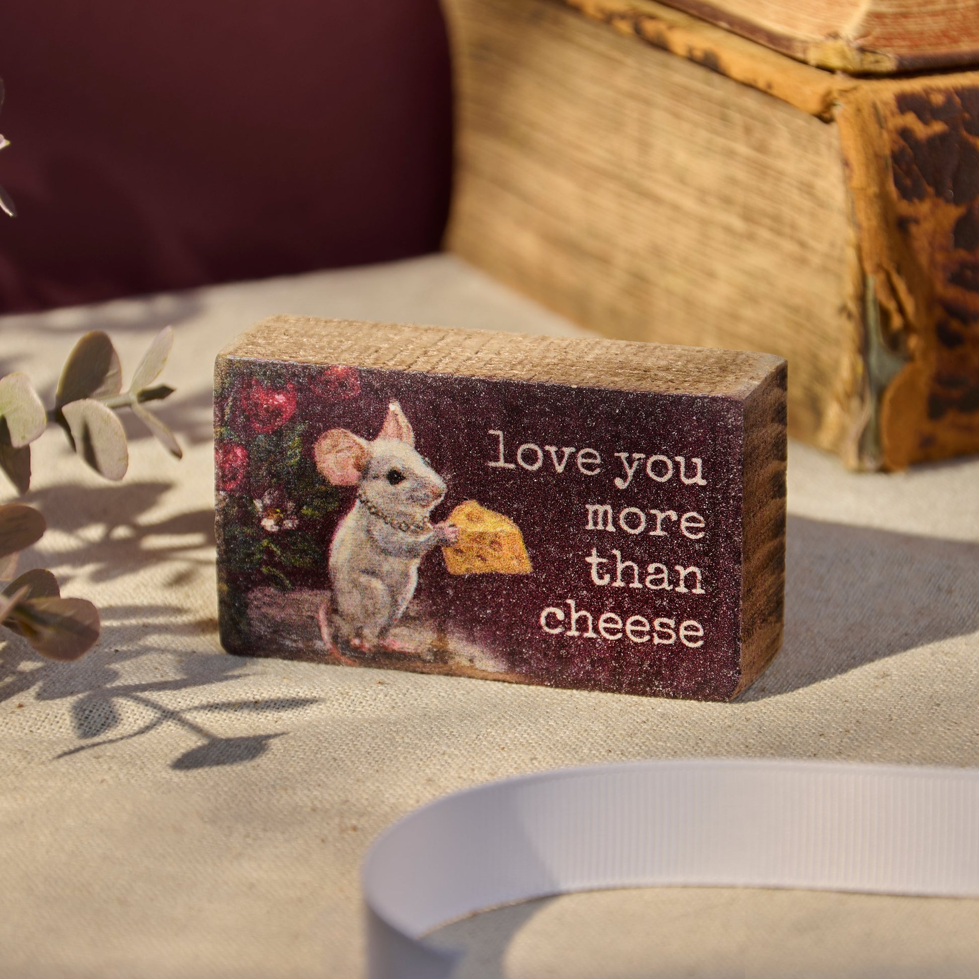 Wooden block with a mouse illustration and 'Love you more than cheese' text on a soft surface.